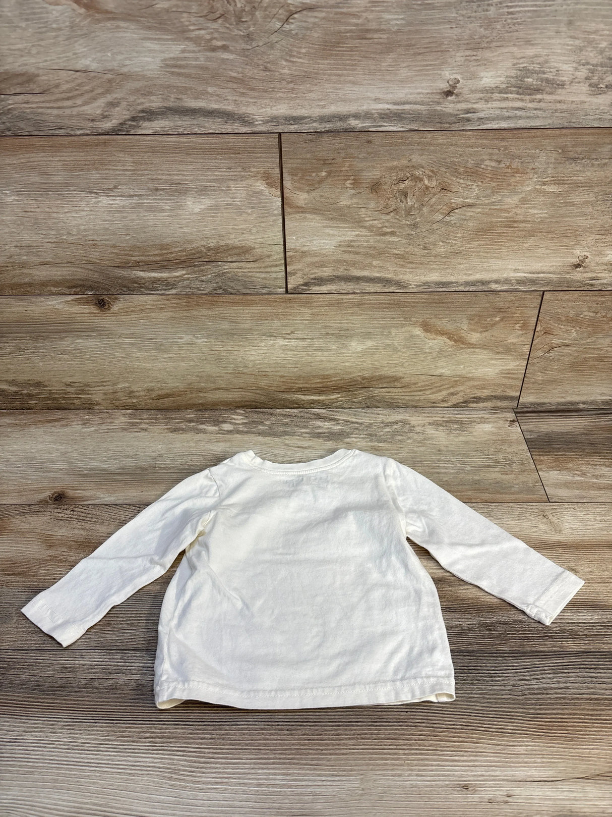 Back view of Disney Jumping Beans long-sleeve infant shirt (12M) showing plain beige back laid flat on wood floor