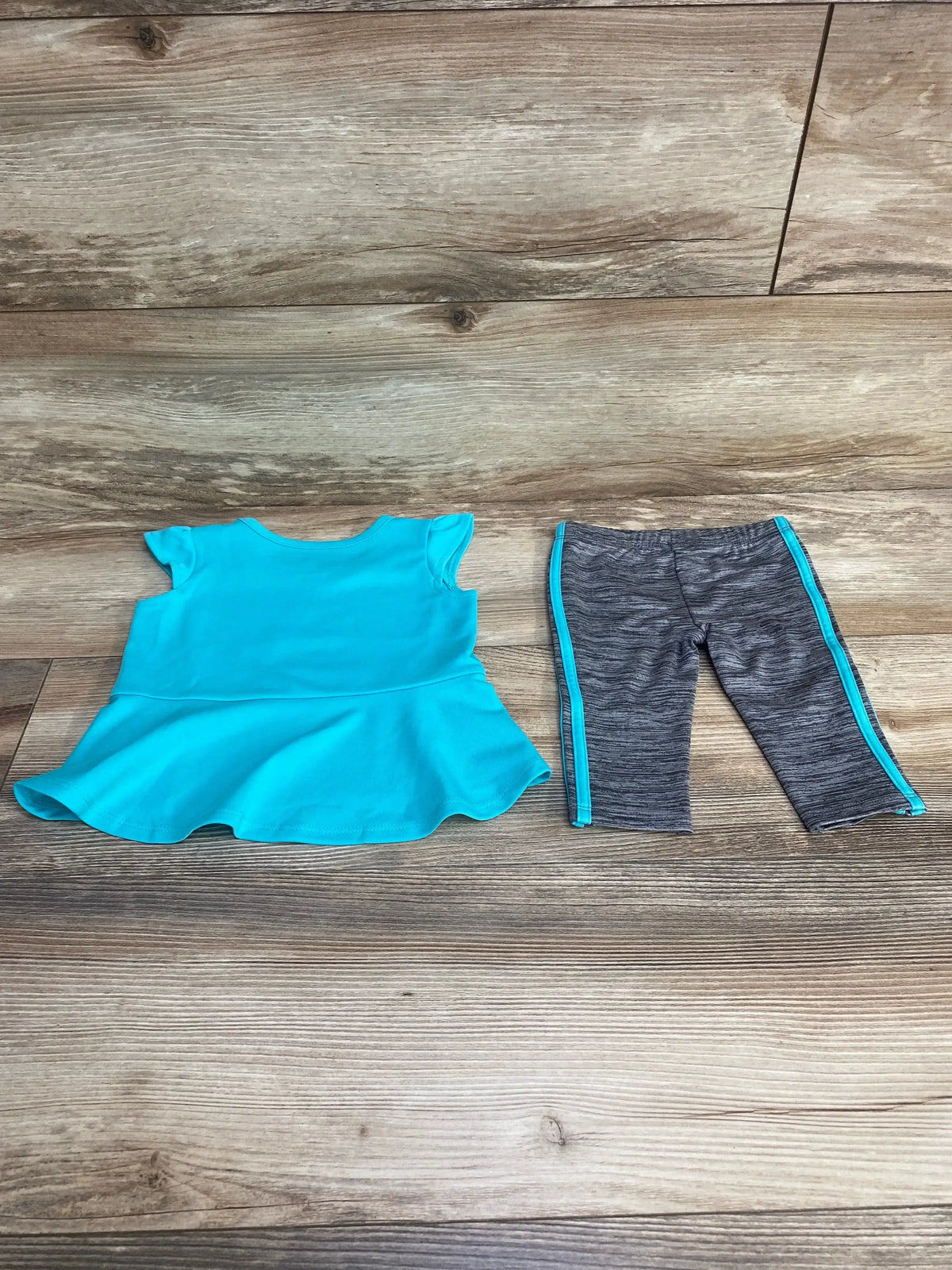 Flat-lay of Adidas baby 2-piece: turquoise peplum top and gray leggings with turquoise side stripes on wood background