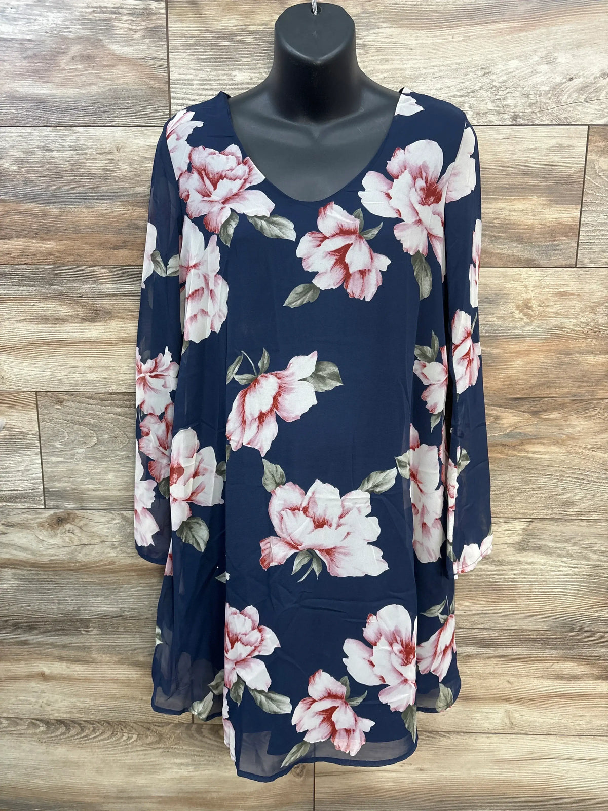Front view of navy maternity V-neck dress with pink and white floral print and sheer long sleeves on wood background