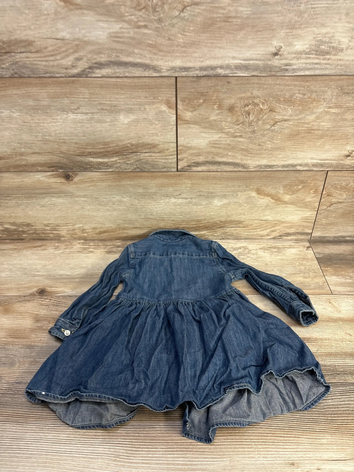 Back view of Ralph Lauren blue denim shirtdress showcasing gathered skirt and long sleeves against a wood-look background