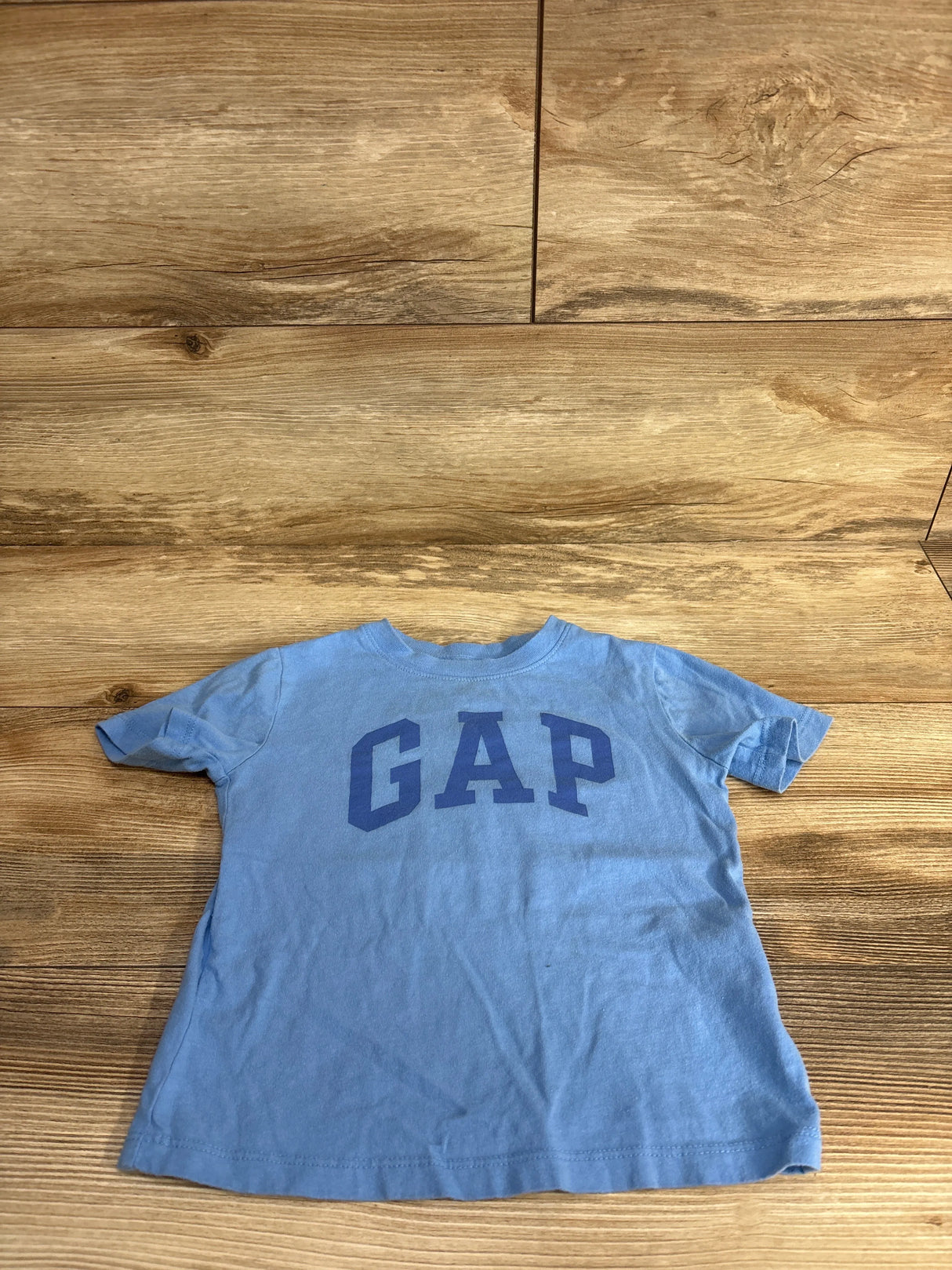 Light blue toddler size GAP t-shirt laid flat on wooden floor with large GAP logo