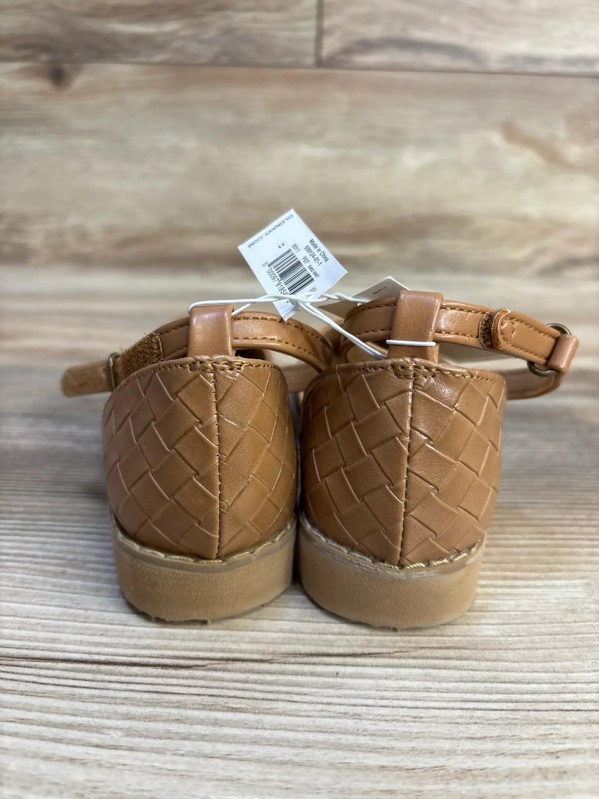 Rear view of woven tan toddler shoes with ankle straps on wood surface
