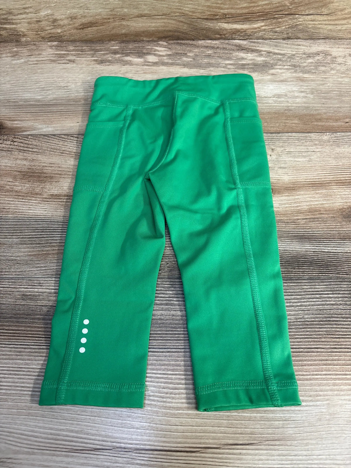 Flatlay of green 3T active leggings showing side pockets and four reflective dots on a wood background