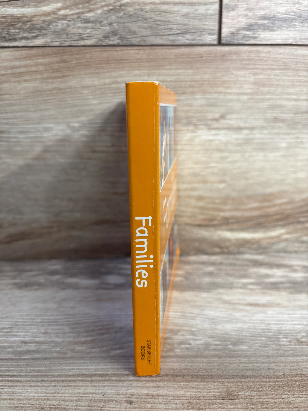 Orange children's book titled Families standing upright on wooden surface with visible spine text