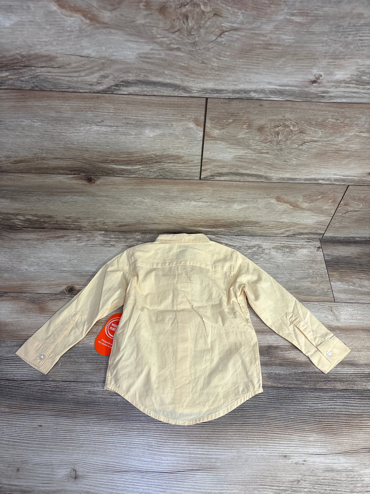Back view of a light yellow long-sleeve button-up shirt on wood floor