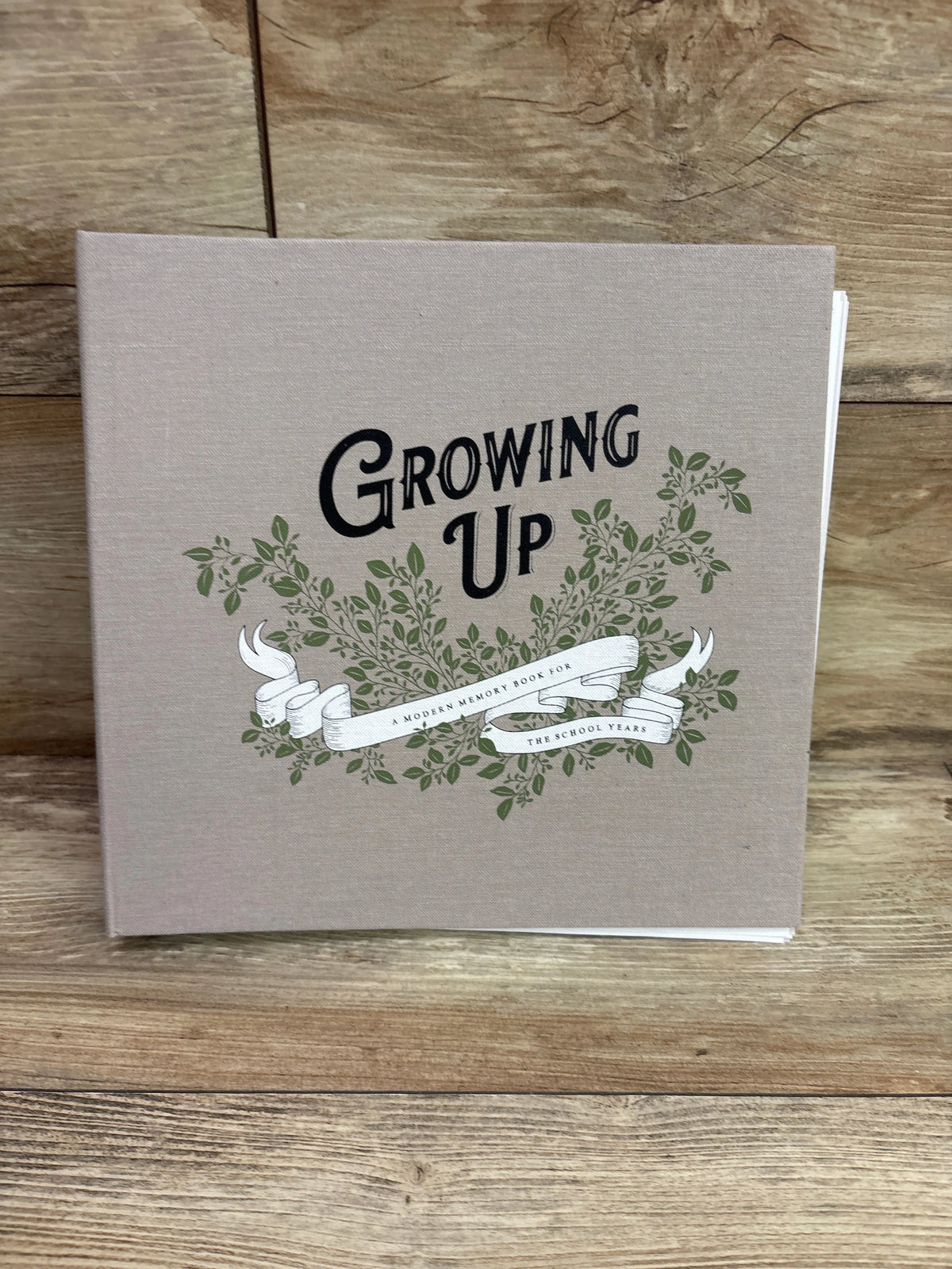 Front cover of Growing Up memory book showing leafy branches and ribbon design on a beige background