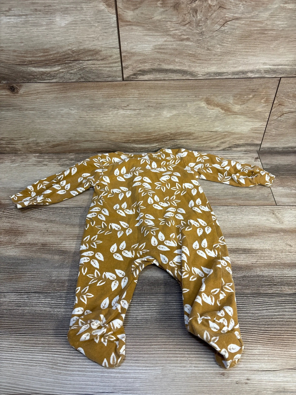 Mustard baby onesie with white leaf print, laid on wood floor