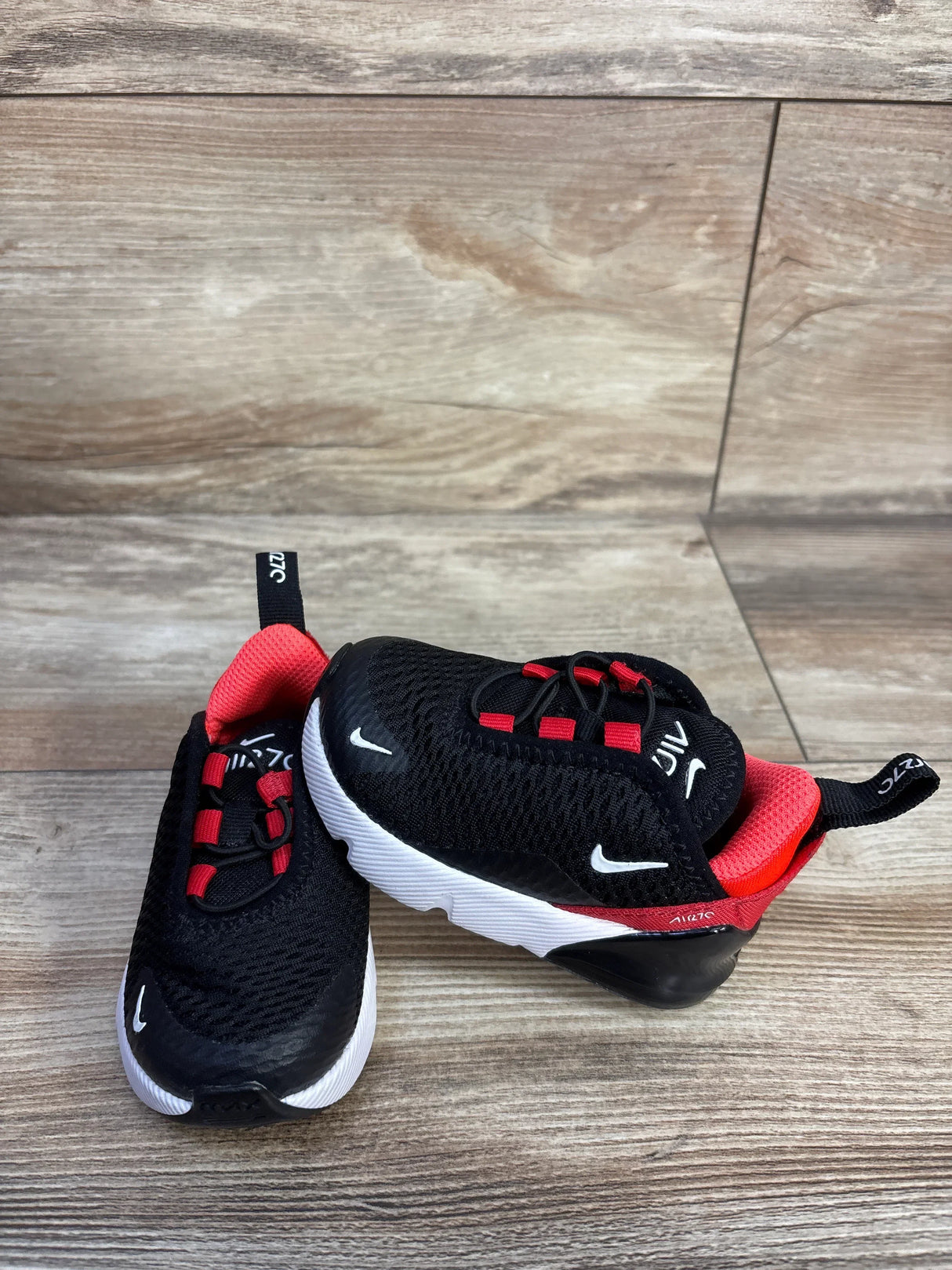 Angled front view of toddler Nike Air Max 270 Bred sneakers, black with red lining and white sole on wood background