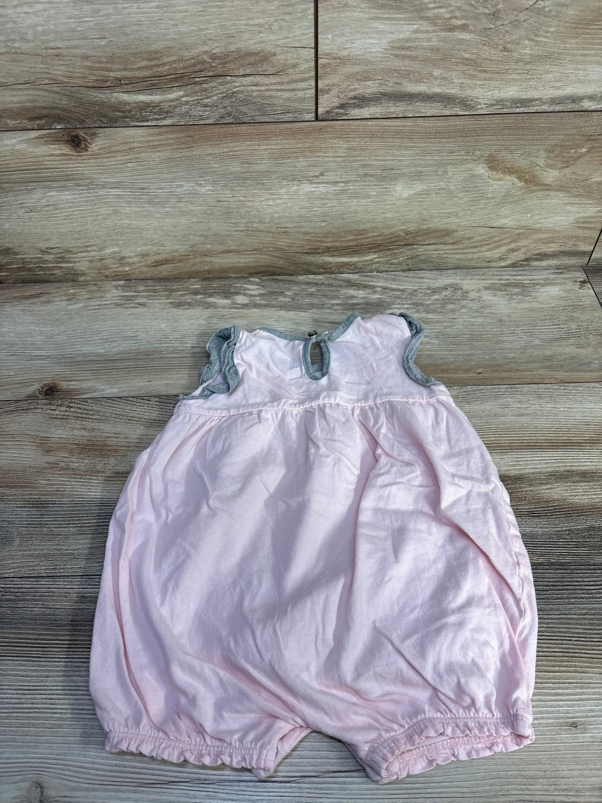 Flat lay of pink Burt’s Bees shortie romper with gray-trim ruffle sleeves and elastic leg openings on wood background