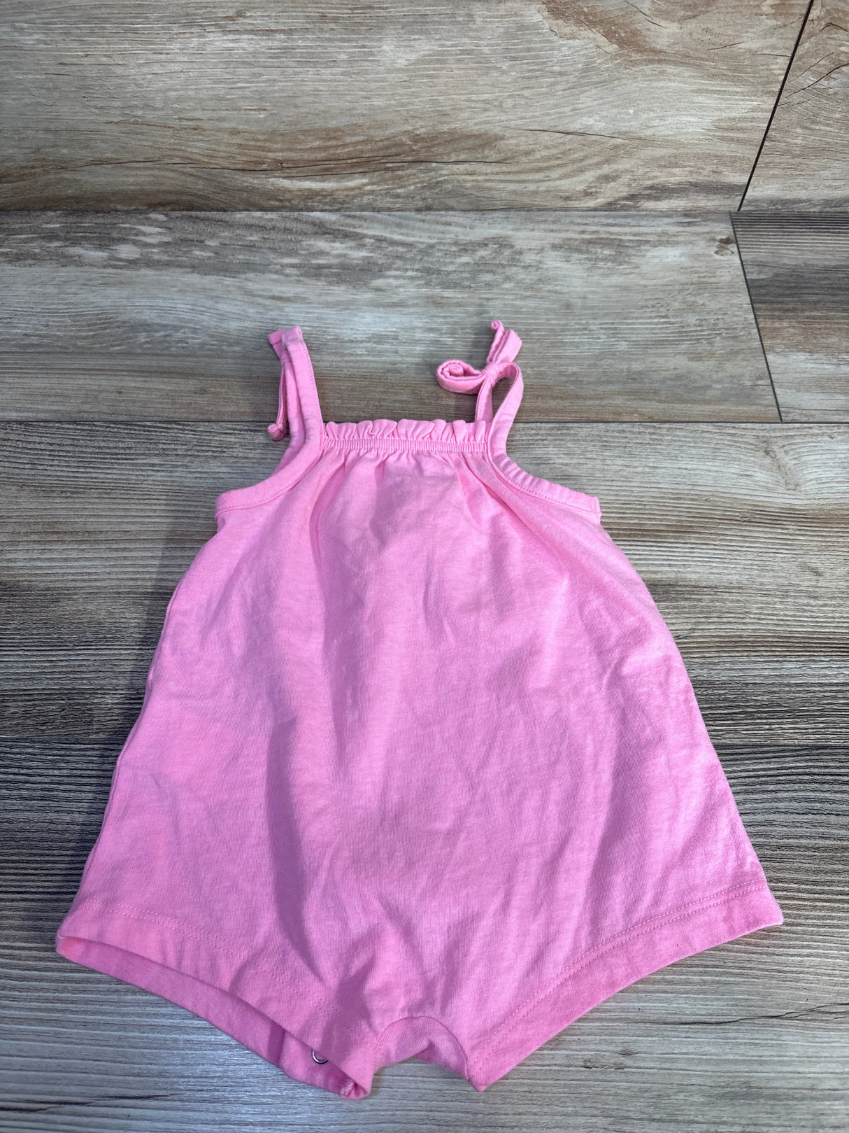 Flat lay of pink Old Navy sleeveless tie-knot shortie romper showing knotted shoulder straps and snap crotch on wood floor