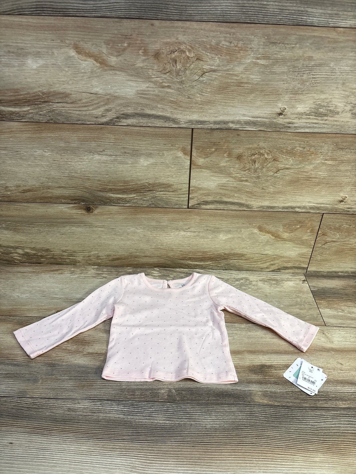 Flat lay of light pink long-sleeve baby shirt showcasing small polka dots on wooden background