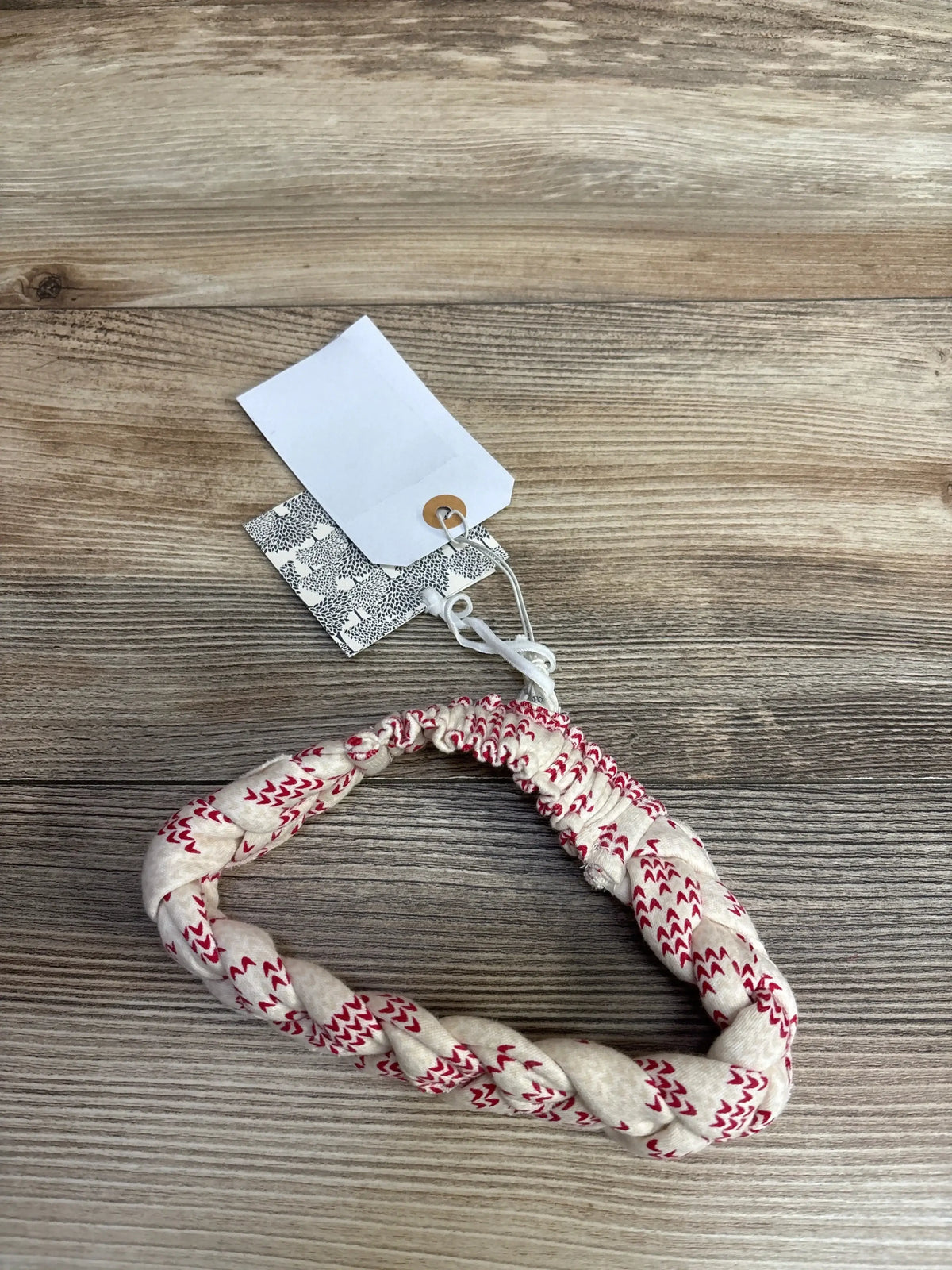 Braided cream and red patterned baby headband with price tags on wooden surface