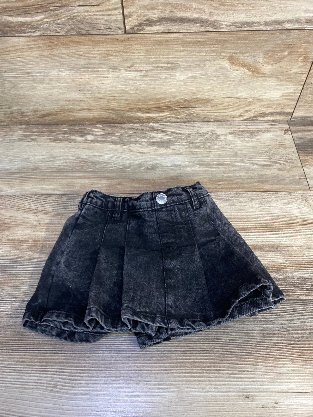 Front view of Nicole Miller black denim skort showcasing fitted waistband and skirt-shorts design on a wood floor