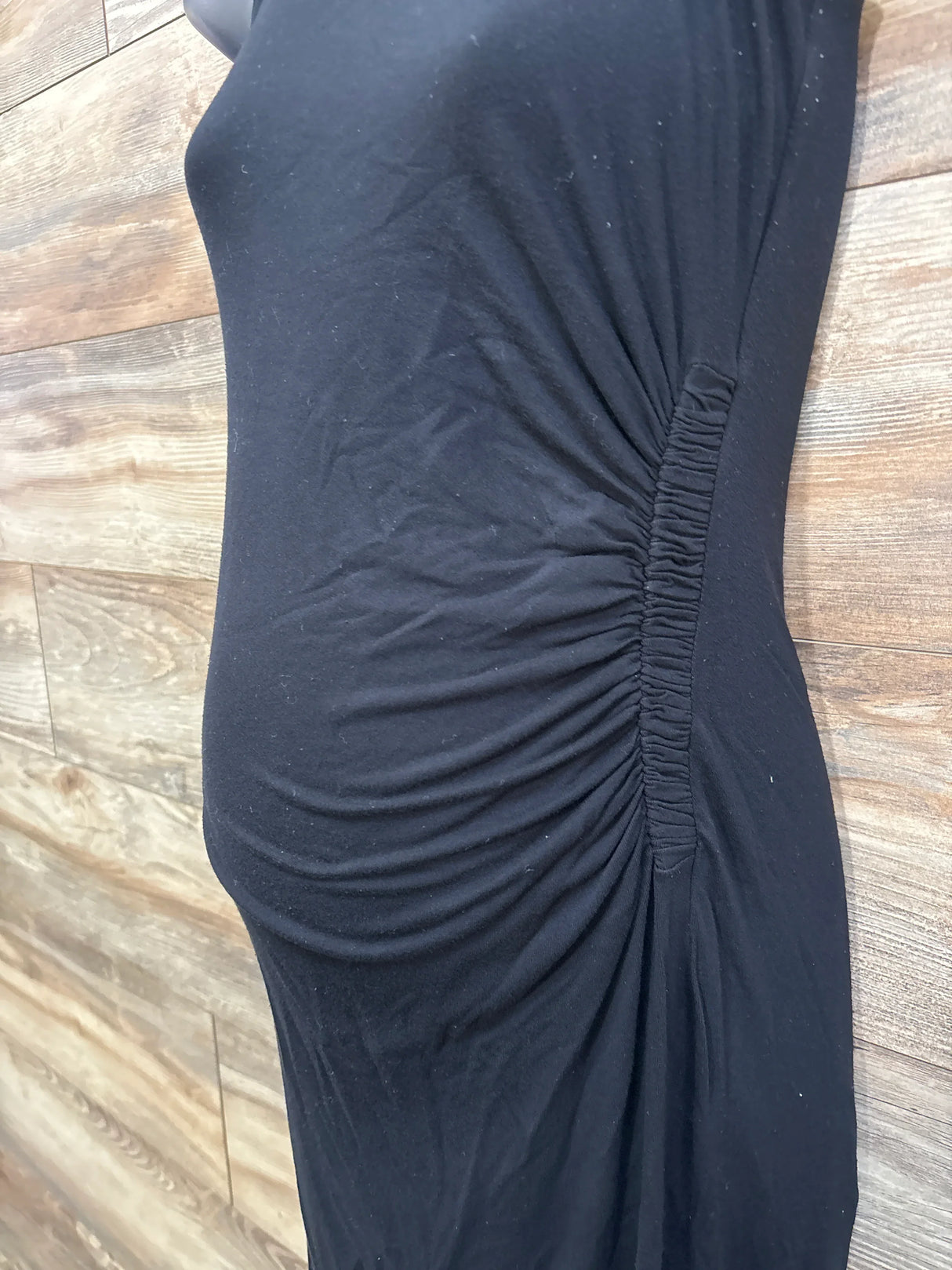 Side view of A Pea In The Pod maternity tank dress showcasing side ruching and fitted belly silhouette on wood floor background
