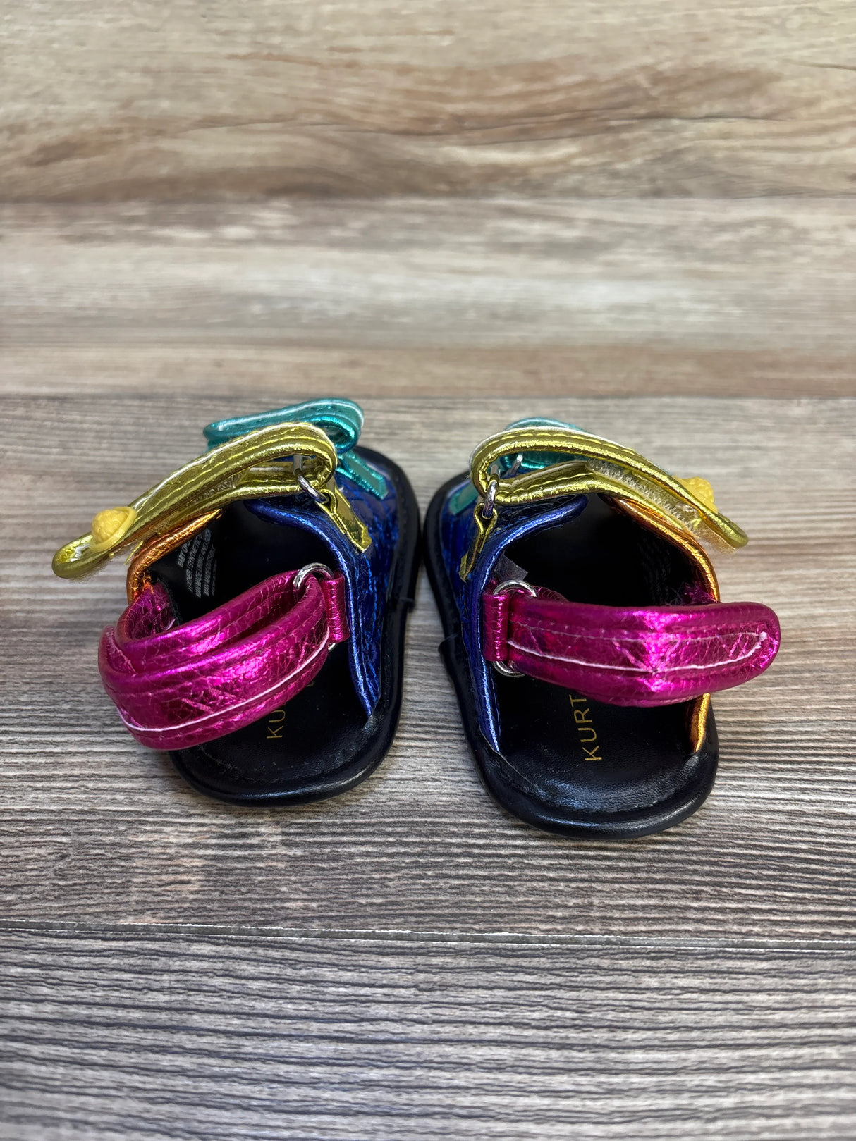 Colorful metallic toddler sandals with hook-and-loop straps on wood background