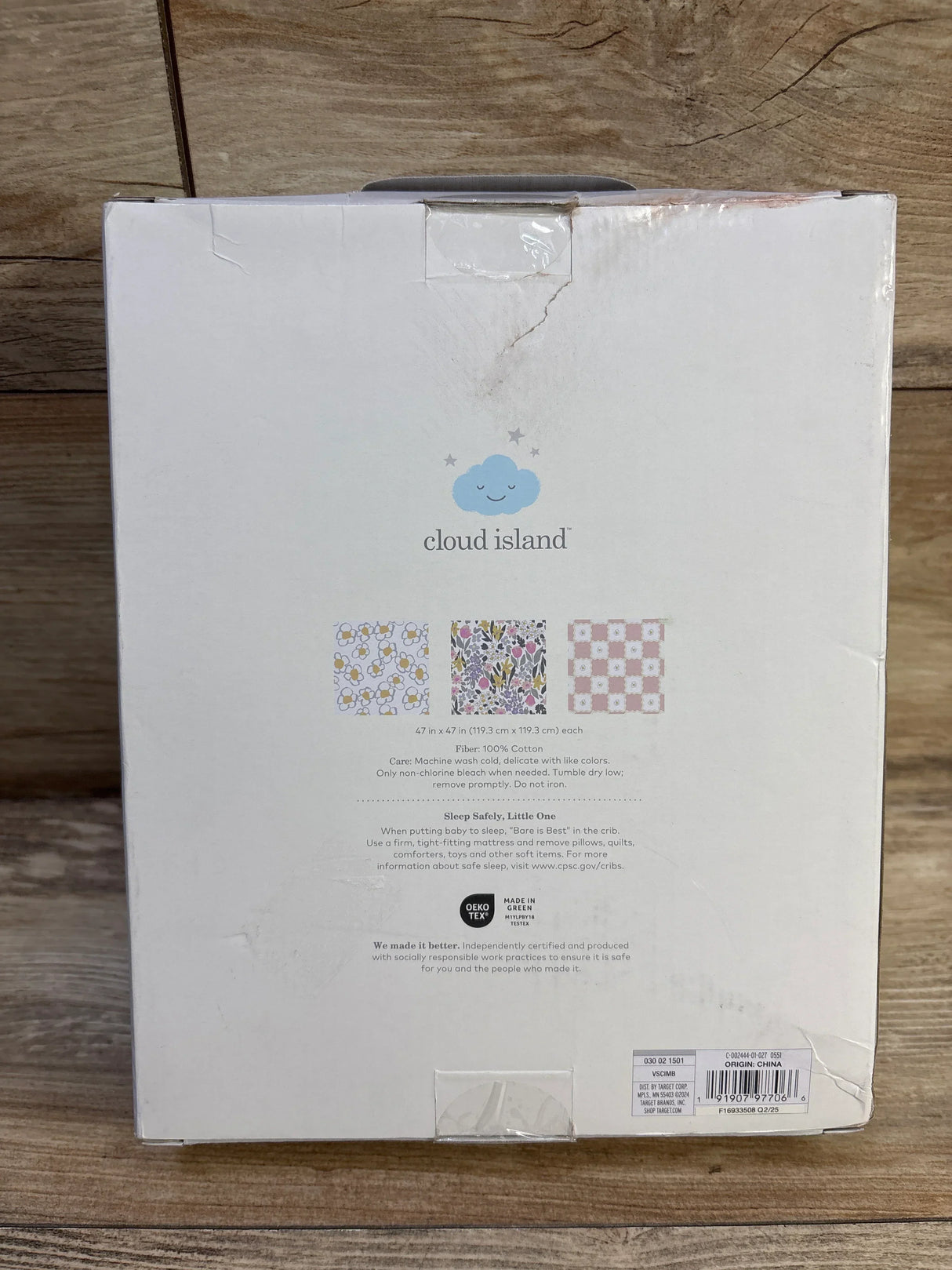Front of boxed Cloud Island 3-pack muslin swaddle blankets showing cloud logo, three pattern swatches, and 47 x 47 in size on wood surface