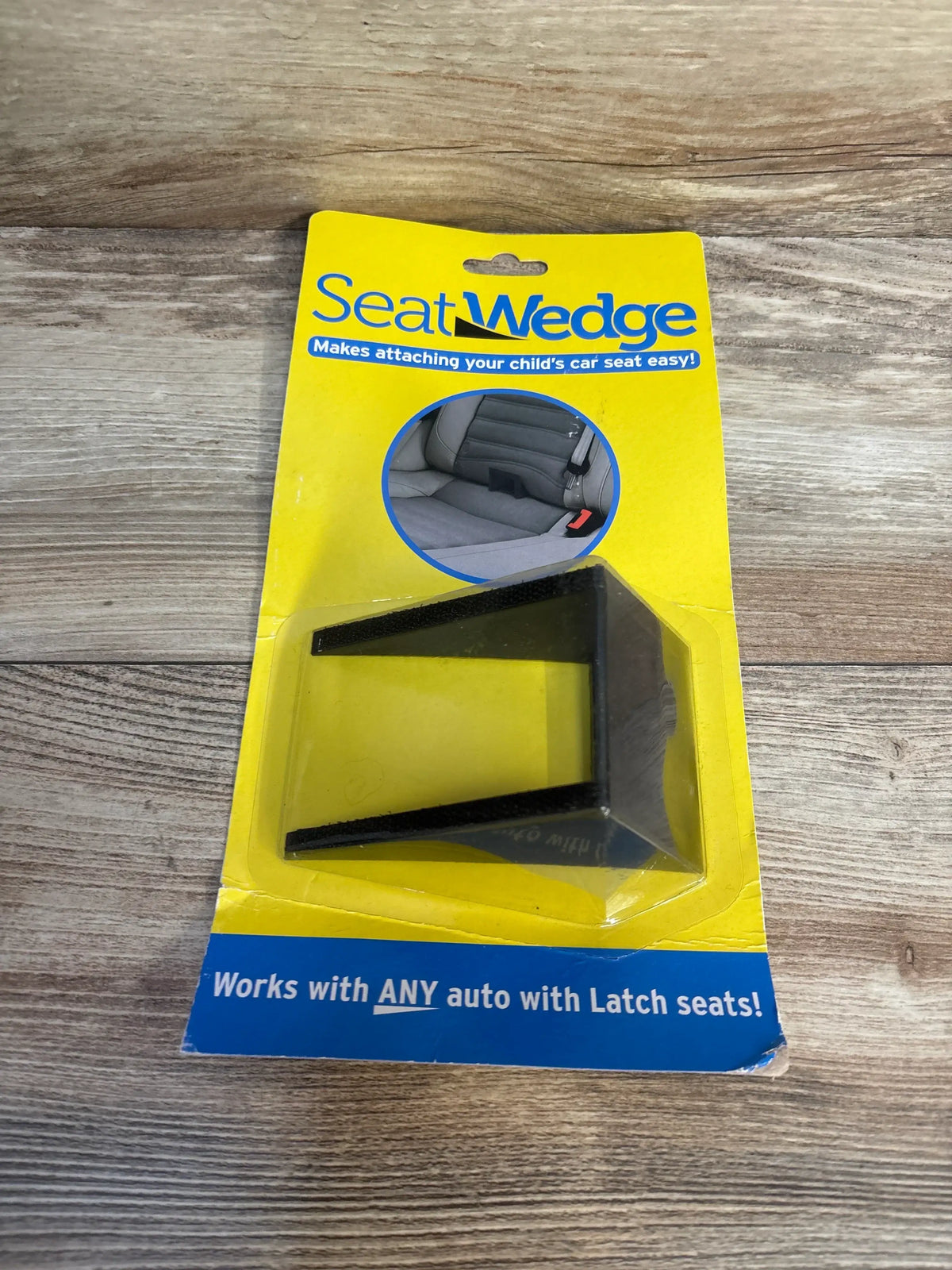 Seat Wedge child car seat accessory in yellow retail packaging, on wood surface.