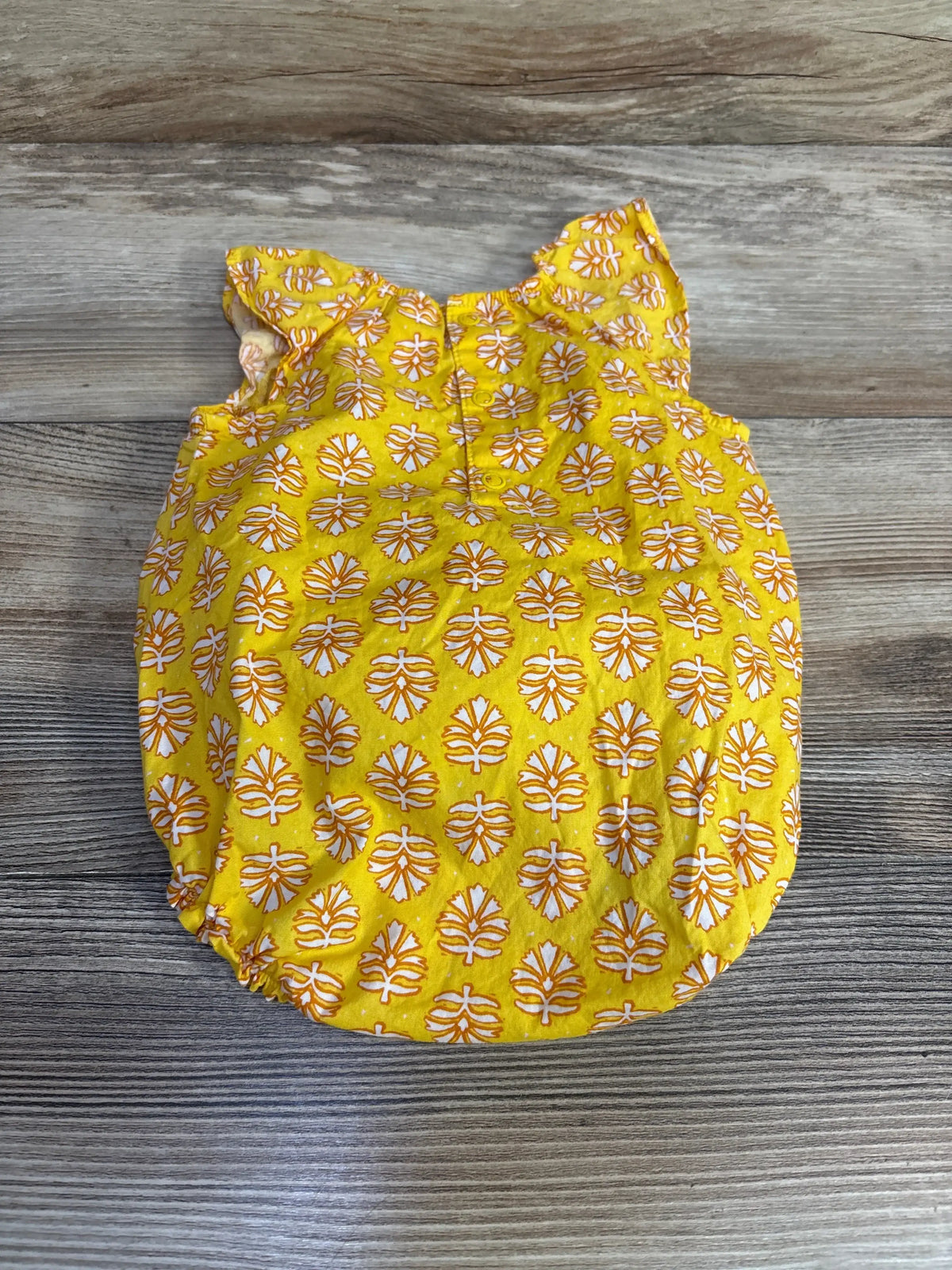 Flat lay of yellow Just One You baby romper showing white and orange leaf print and ruffle sleeves on wood floor