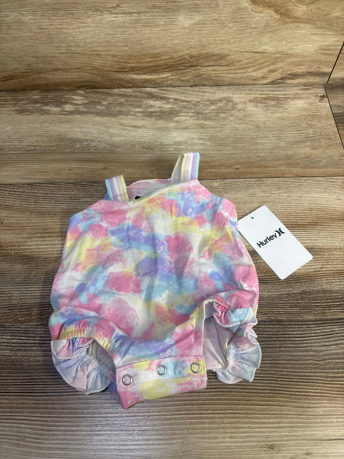 Front view of Hurley butterfly bubble romper in pink showcasing flutter sleeves and snap closures on a wood-grain background