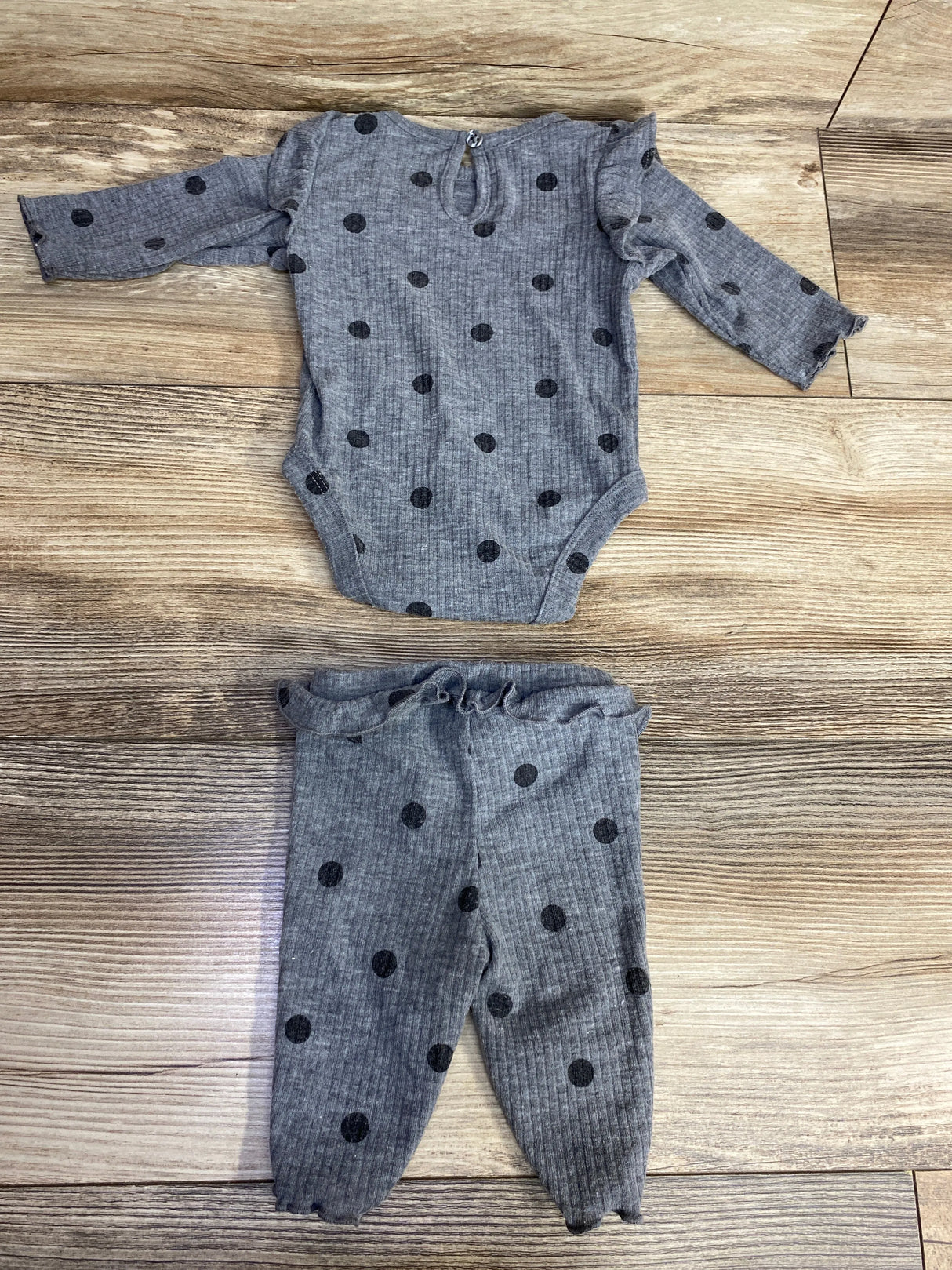 Gray baby outfit with black polka dots, long-sleeve onesie and matching pants on wood floor