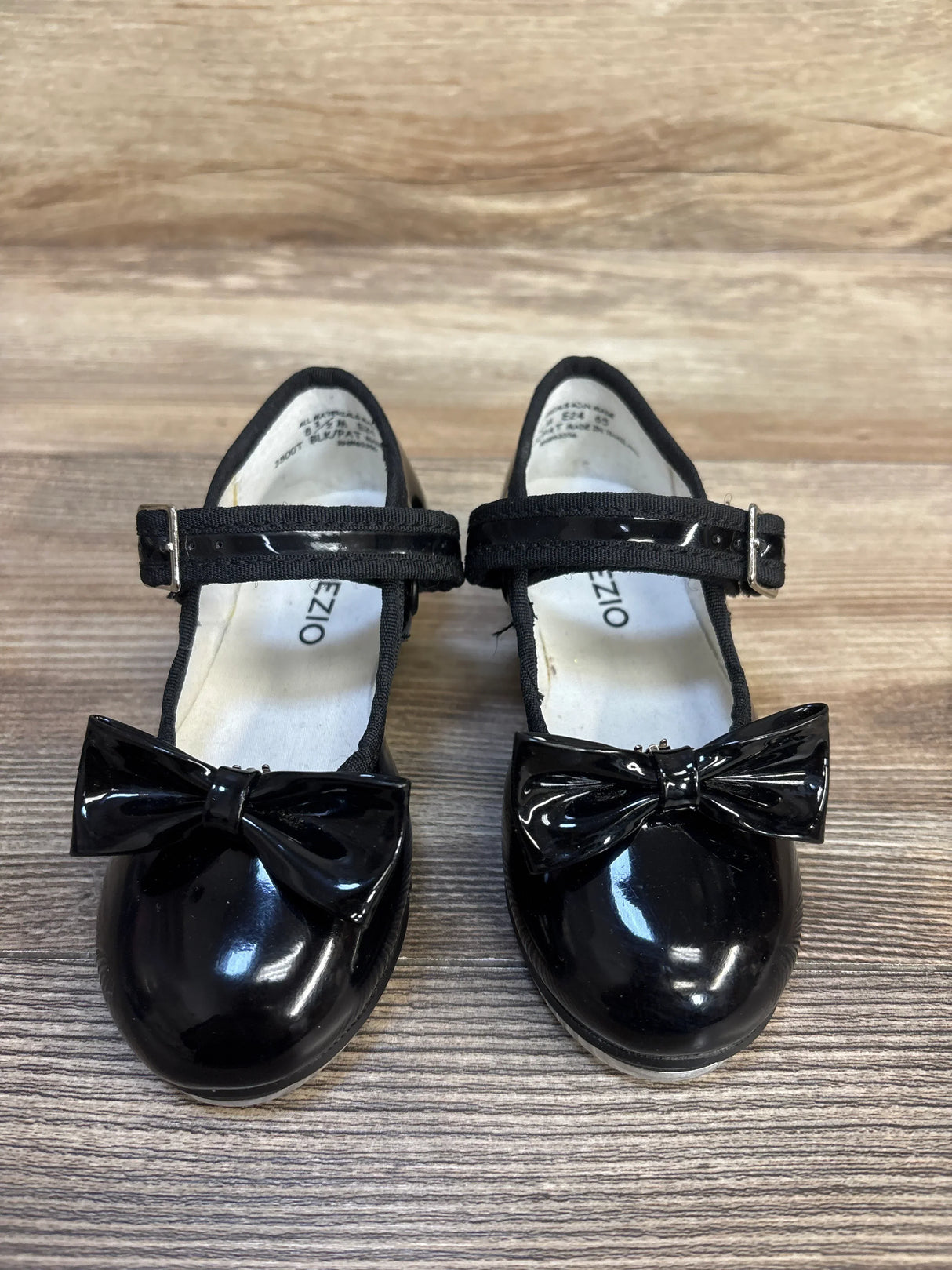 Black patent leather girls Mary Jane shoes with bows on wooden floor