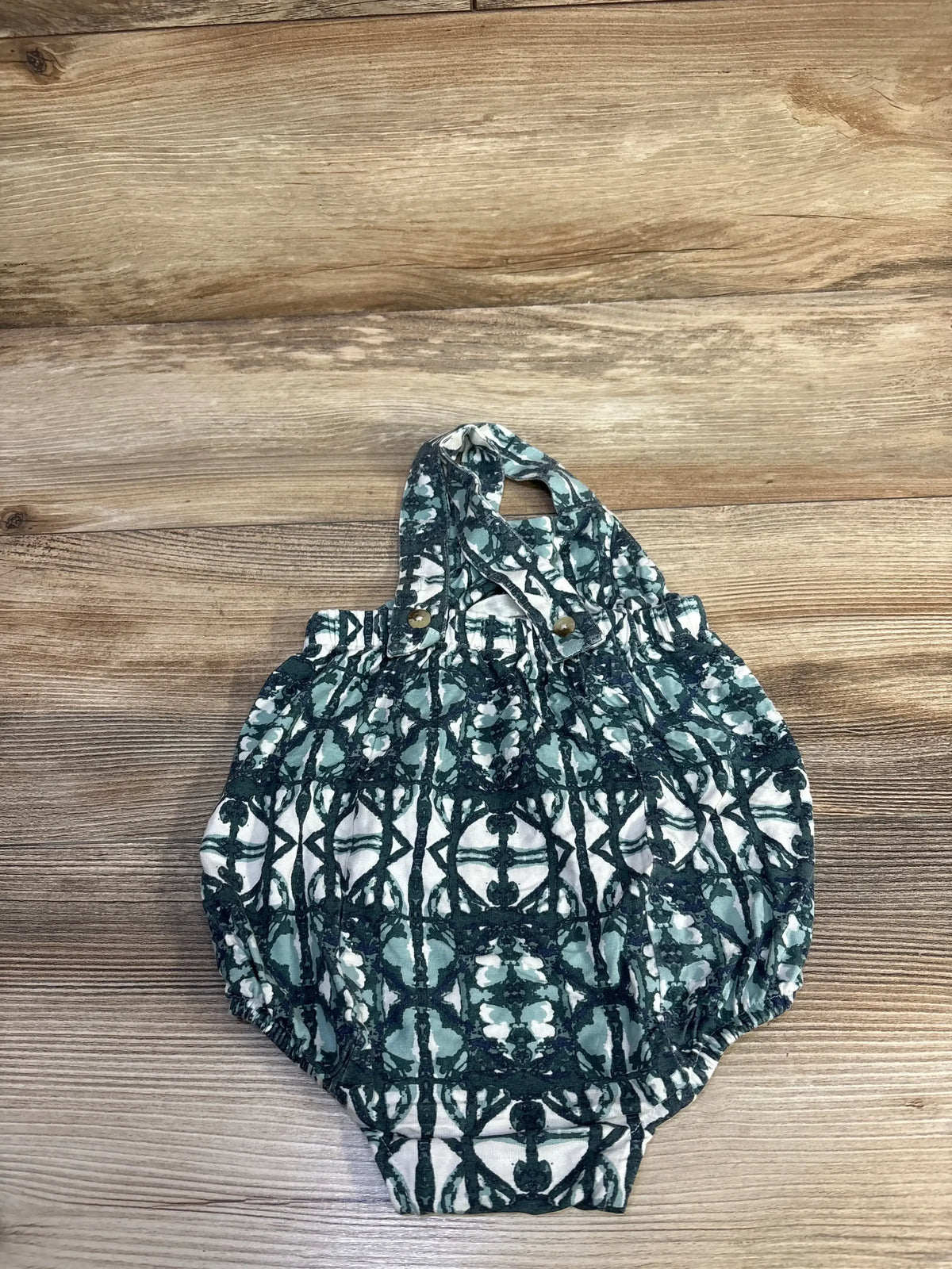 Flat lay of sleeveless bubble romper (12–18m) with green geometric print and button shoulder straps on wooden background