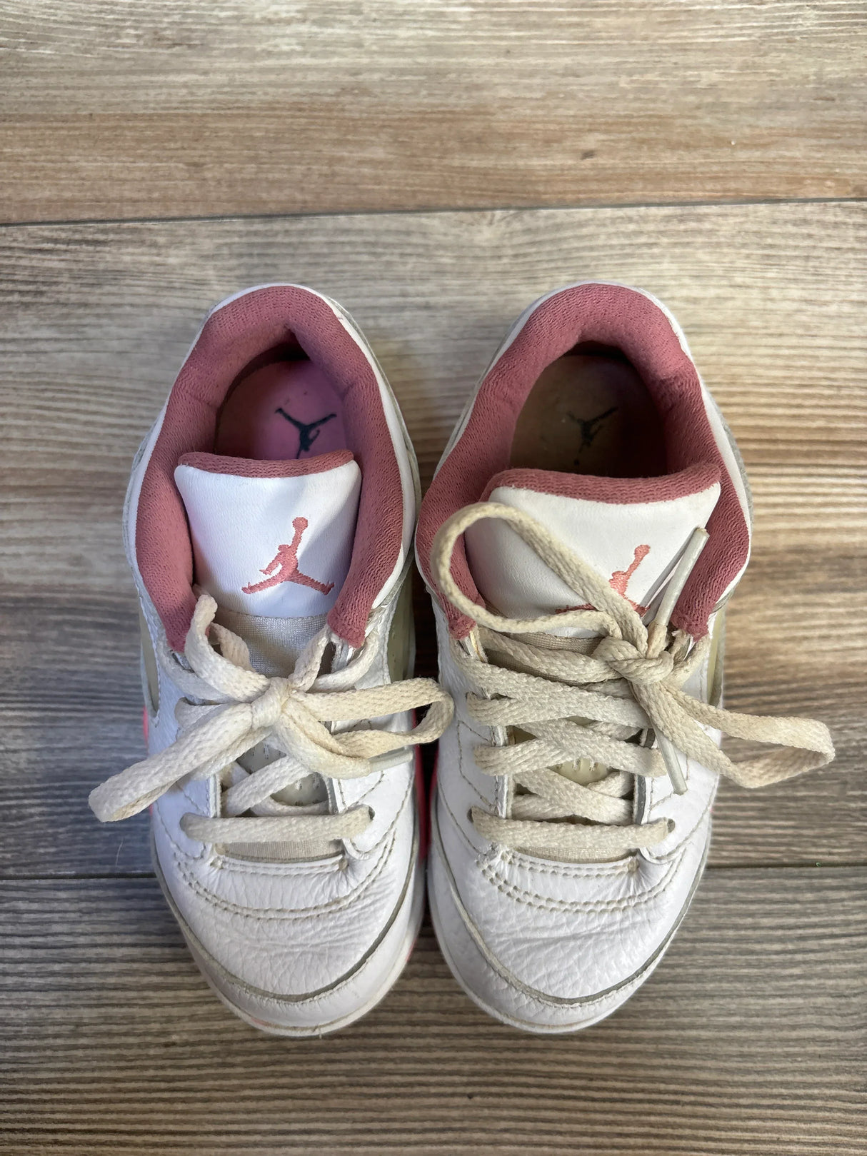 Top-down view of Air Jordan 5 Retro Low TD “Crafted For Her” toddler sneakers, white leather with pink inner lining, Jumpman logo on tongue and tied laces on wood floor