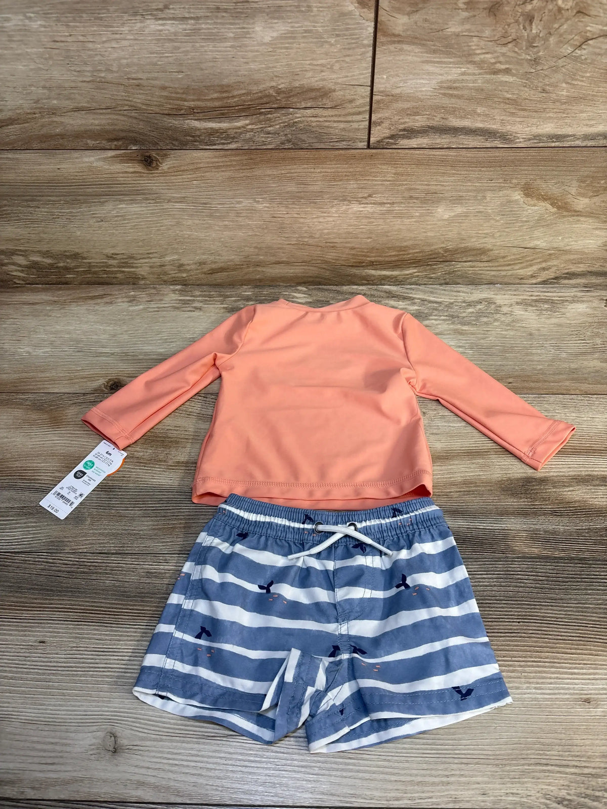Peach long sleeve swim top and blue striped kids swim shorts on wood background