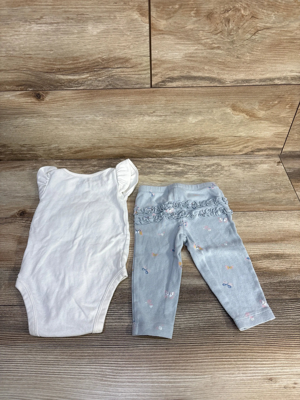 Top-down view of Carter’s 6-month two-piece baby outfit showing a white flutter-sleeve bodysuit and butterfly-patterned pants on wood