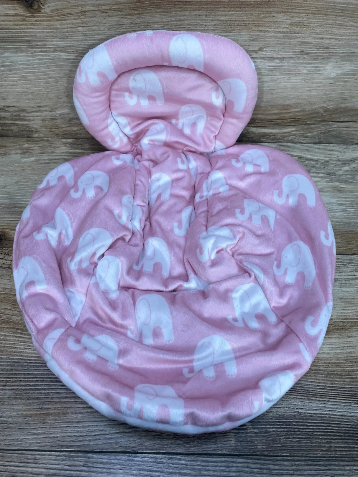 Overhead view of reversible swing insert in pink with white elephant print, padded head support on wood floor