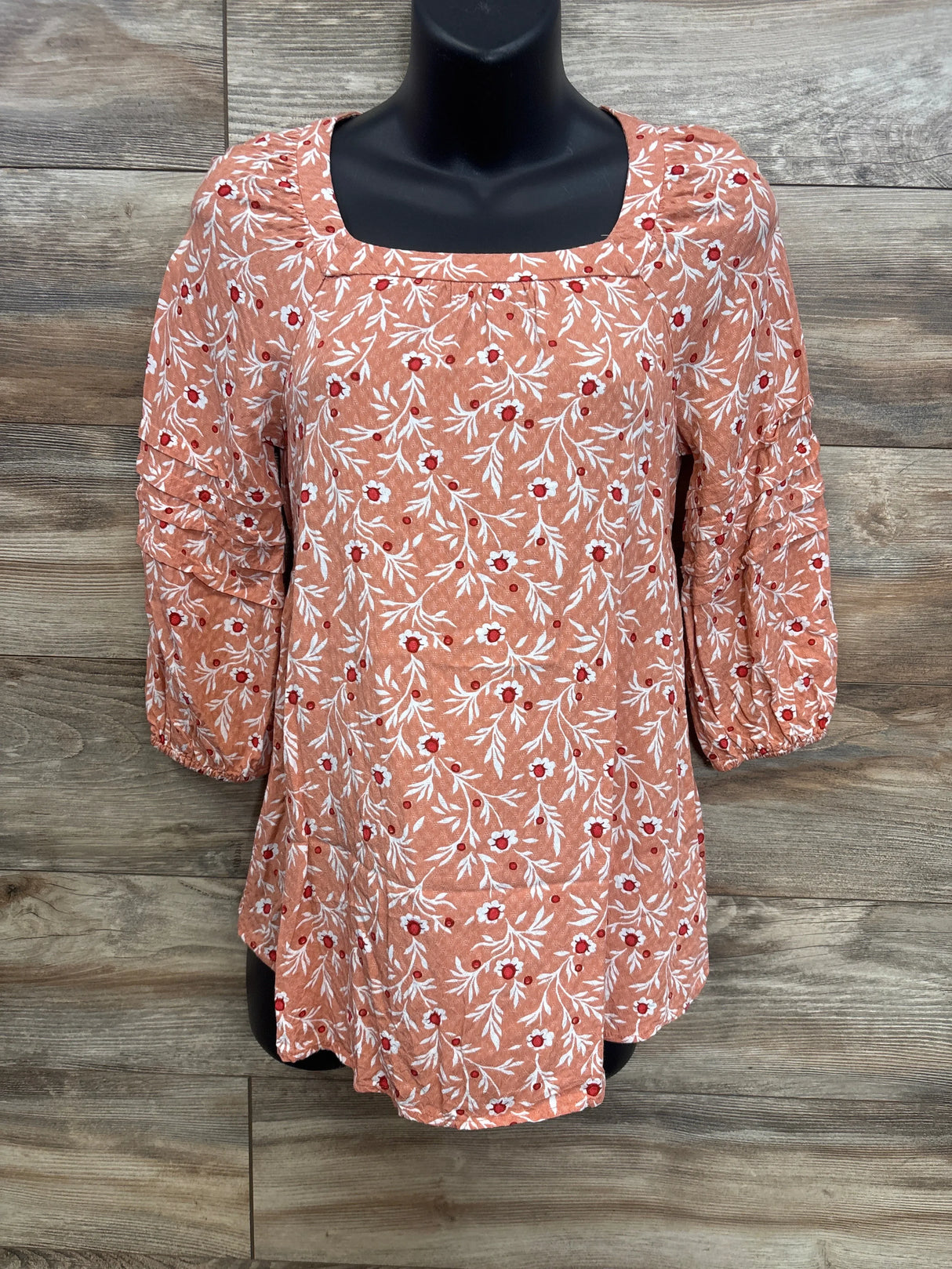Front view of orange maternity floral blouse showing square neckline, ruched three-quarter sleeves and white-red floral print on wood background