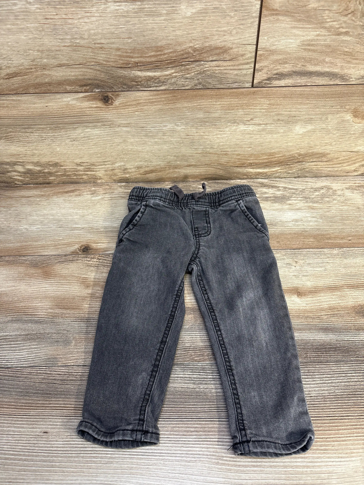 Front view of Oshkosh drawstring jeans in grey showcasing adjustable drawstring waist and front pockets on a wood-look floor