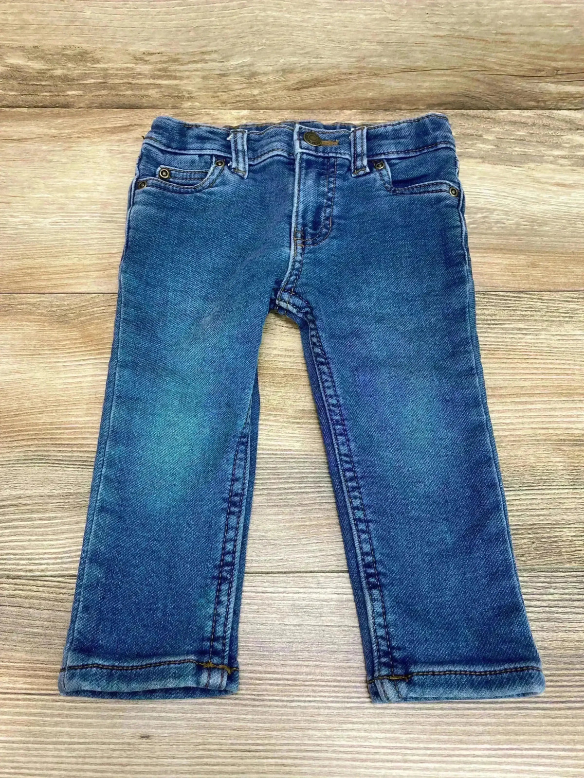 Front flat lay of Carter’s blue skinny toddler jeans, size 18M, showing faded knees and rolled hems on wood background
