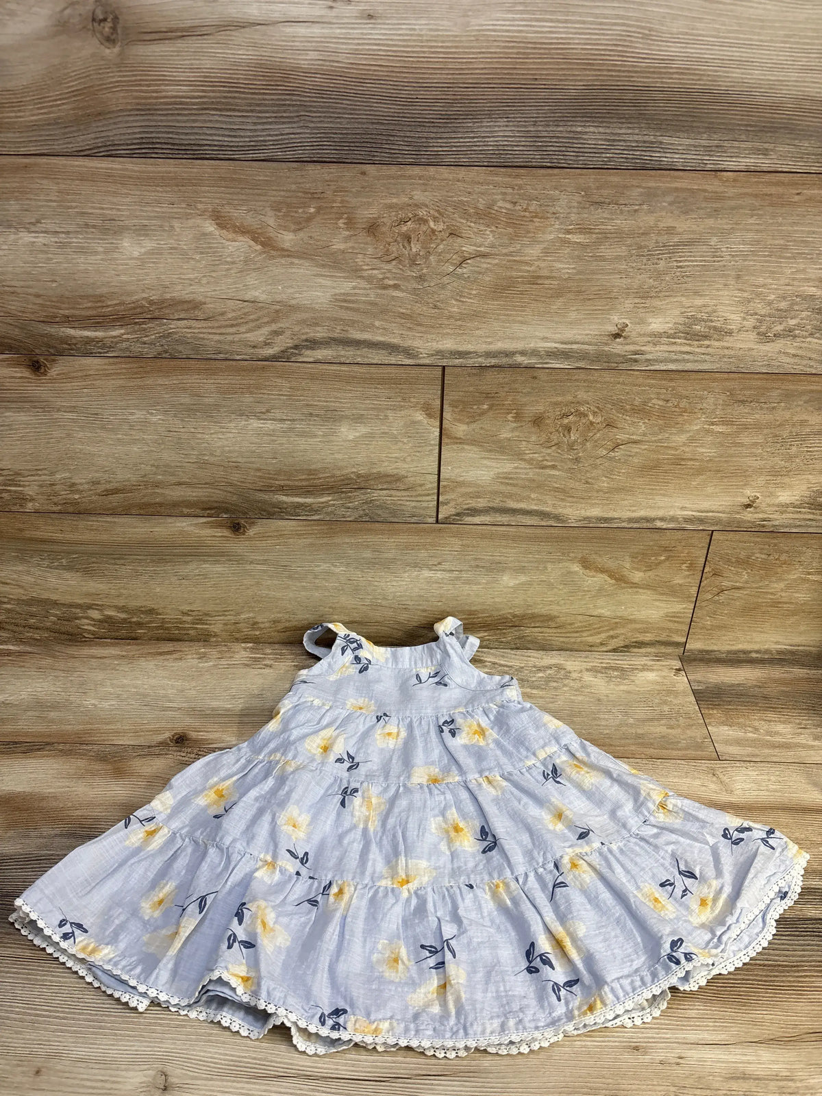 Flat lay of blue floral tiered toddler dress size 4T showcasing ruffled tiers and lace trim on wood background