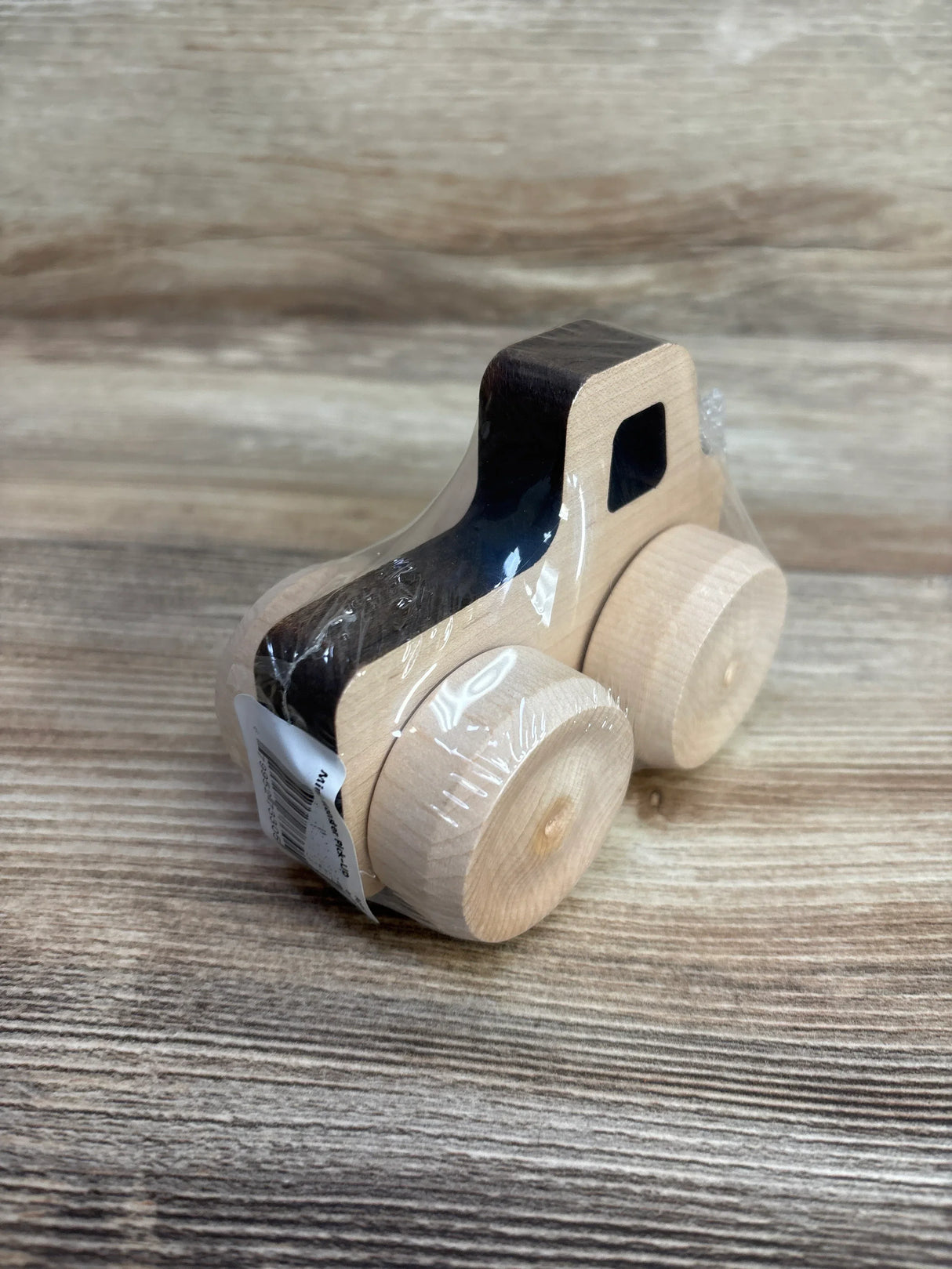 Three-quarter view of Maple Landmark Mini Monster Pickup wooden car showing black-painted cab, natural maple body, round wheels, plastic wrap on wood-grain surface