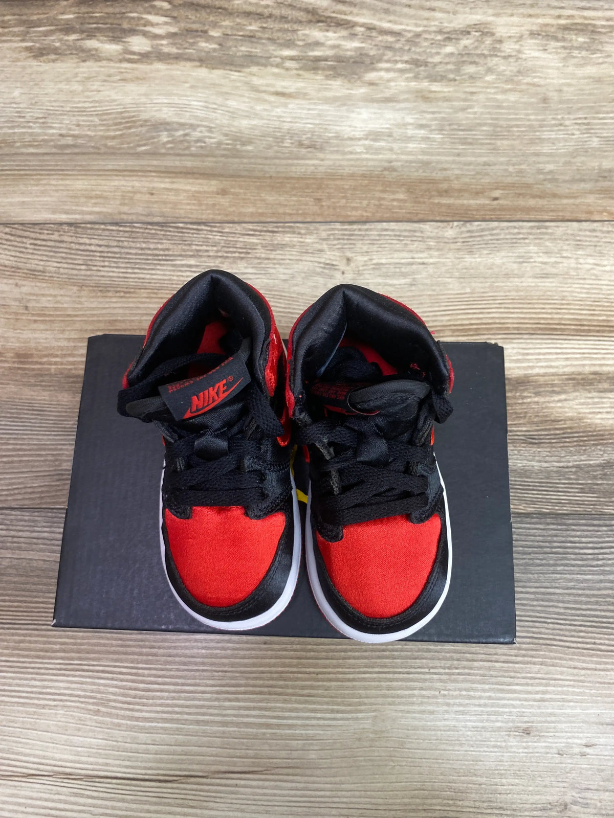 Top view of Air Jordan 1 Retro High OG TD Satin Bred sneakers showcasing red and black panels on a black shoebox