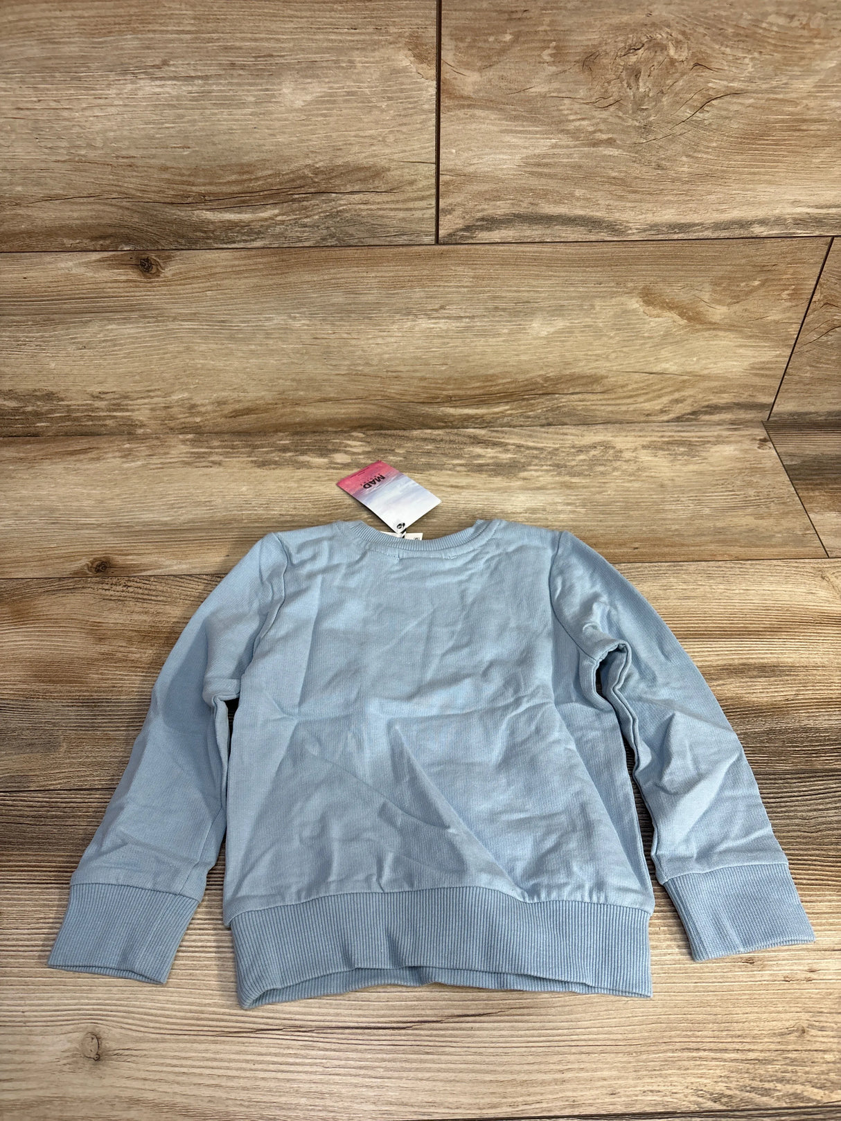 Light blue long sleeve sweatshirt with tag on wooden floor background