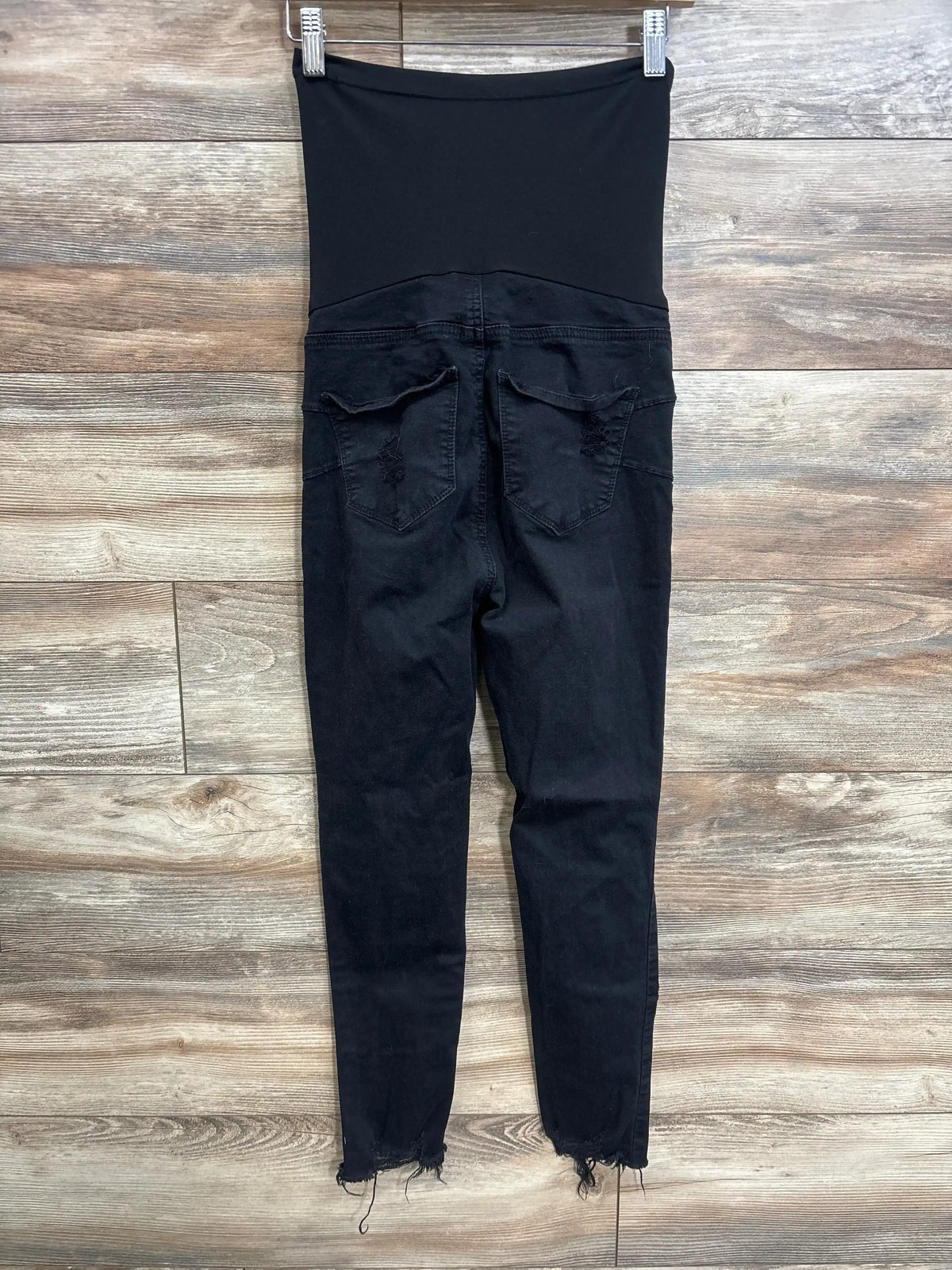 Back view of SONG maternity full panel jeans in black with distressed raw hem on wood plank floor