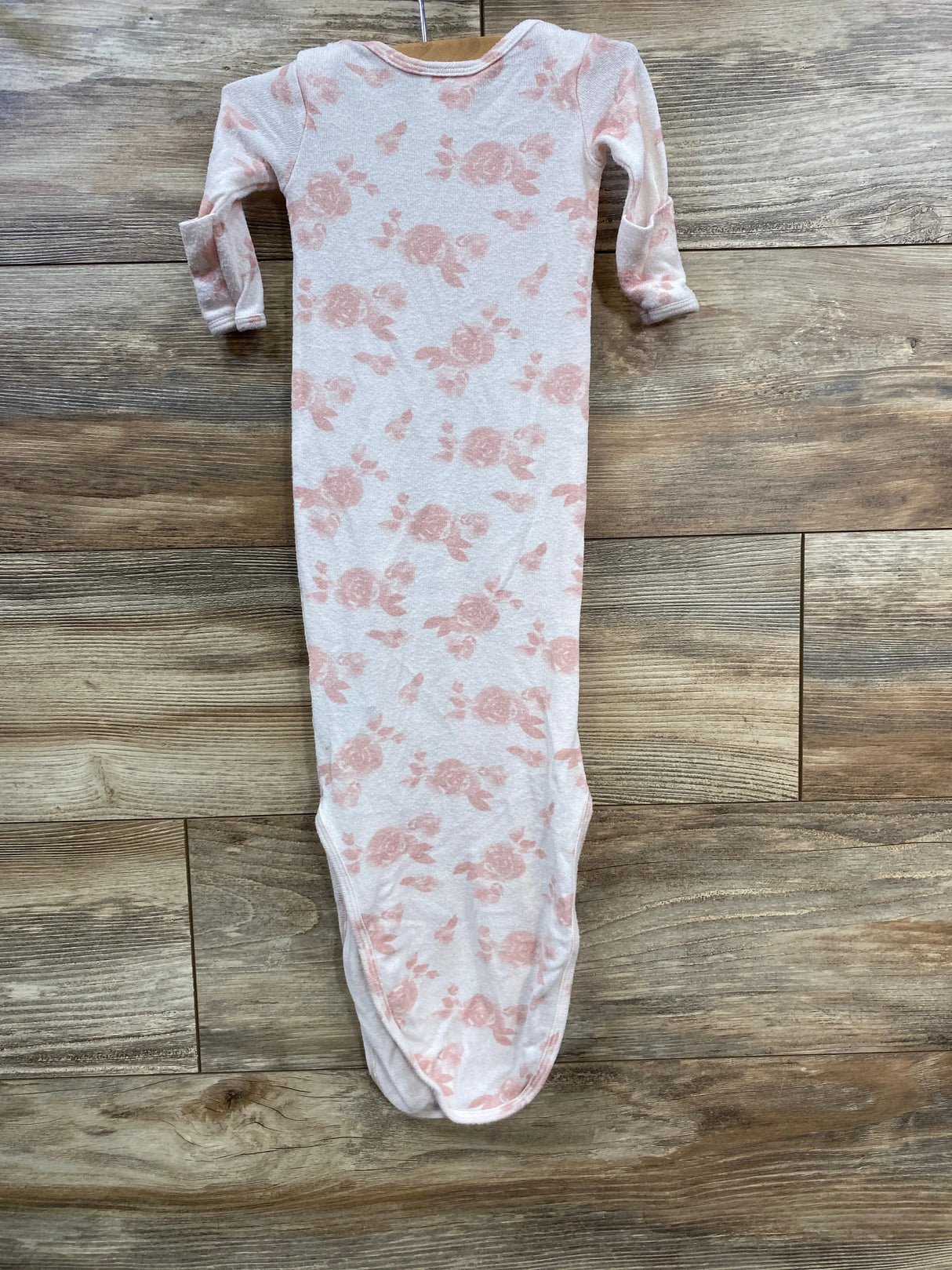 Long-sleeve baby gown with pink floral print on white fabric laid on wooden floor