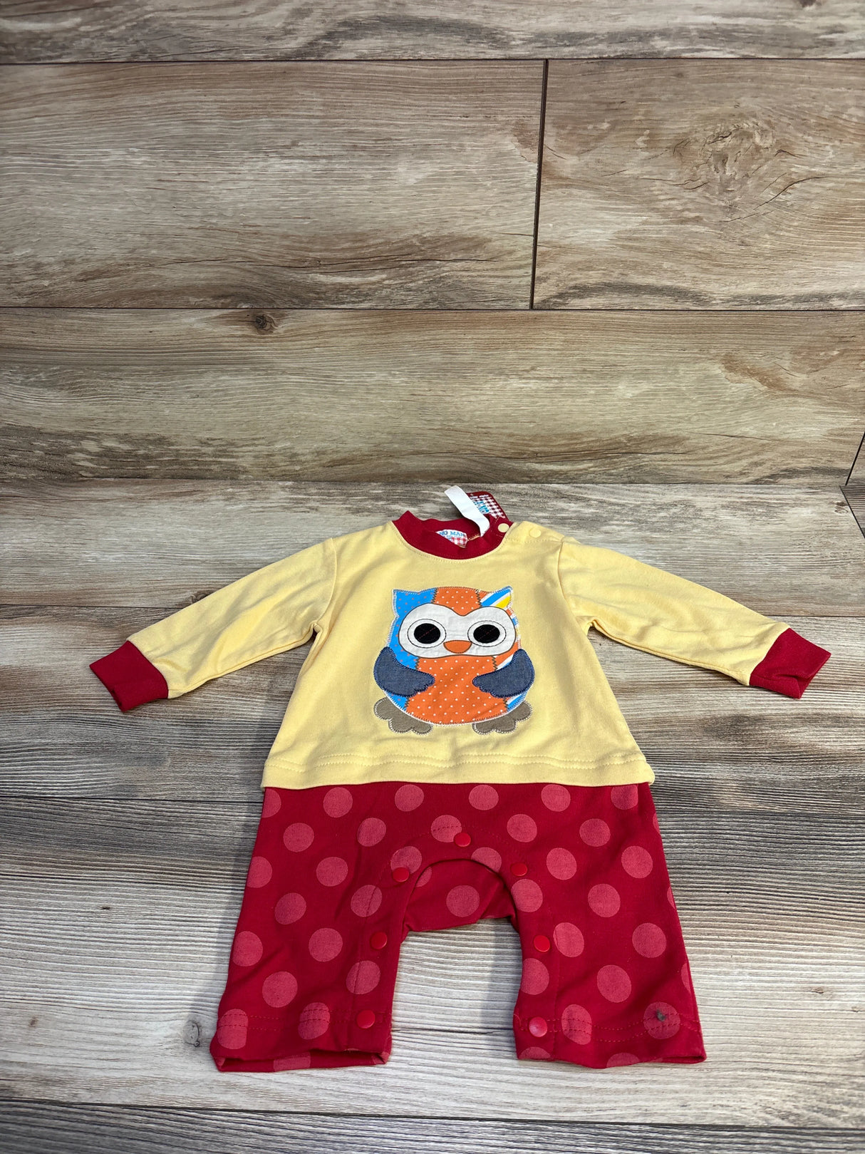 Front flat lay of yellow baby coverall (6-9 months) showing owl appliqué and red polka-dot legs on wood floor