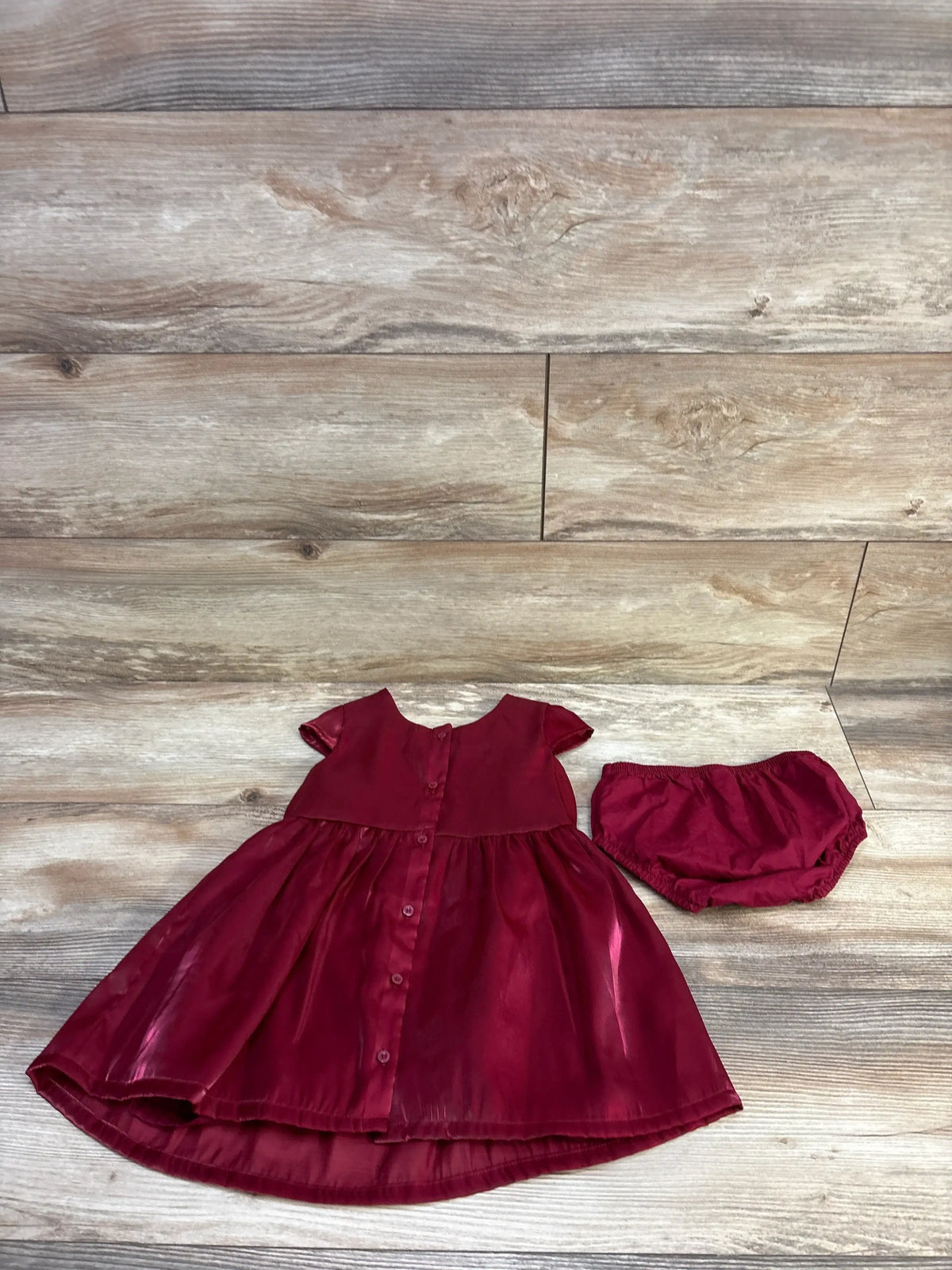 Front flat lay of Just One You red 2-piece dress and bloomers showcasing button-front bodice, short sleeves, and gathered skirt on light wood background