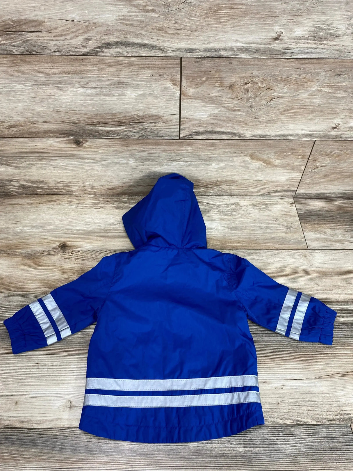 Back view of blue toddler hooded windbreaker with reflective stripes on sleeves and hem on wood floor, size 12M