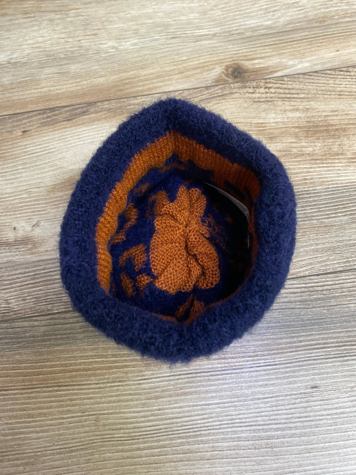 Top view of a navy blue and orange knitted hat with floral pattern on a wooden floor