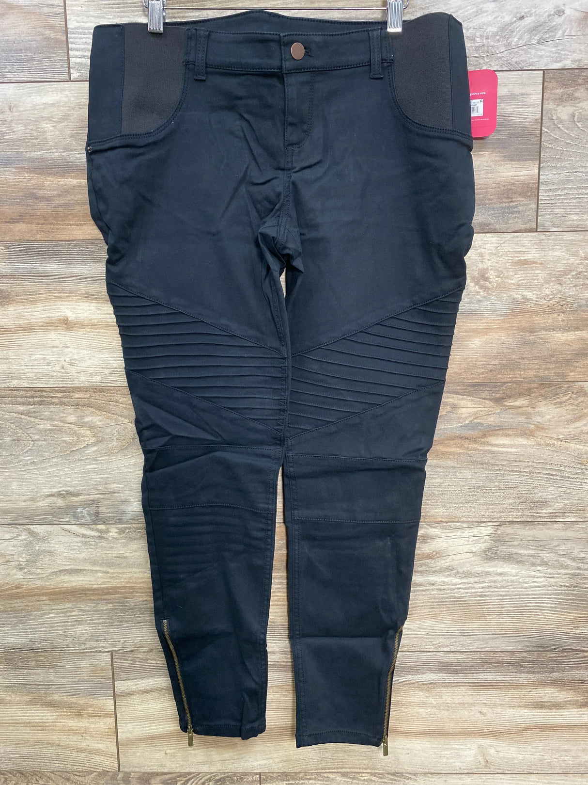 Black moto biker pants with ribbed knee panels and ankle zippers on wooden floor