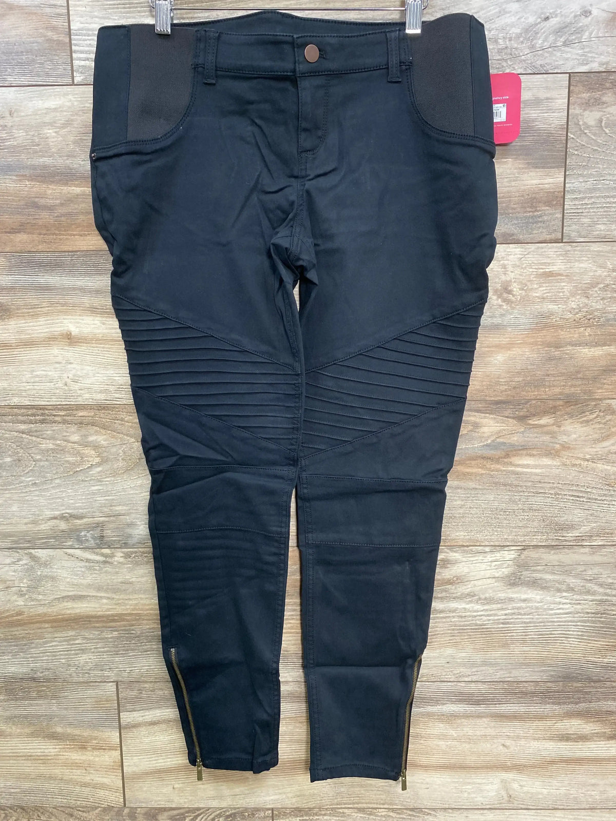 Black moto biker pants with ribbed knee panels and ankle zippers on wooden floor