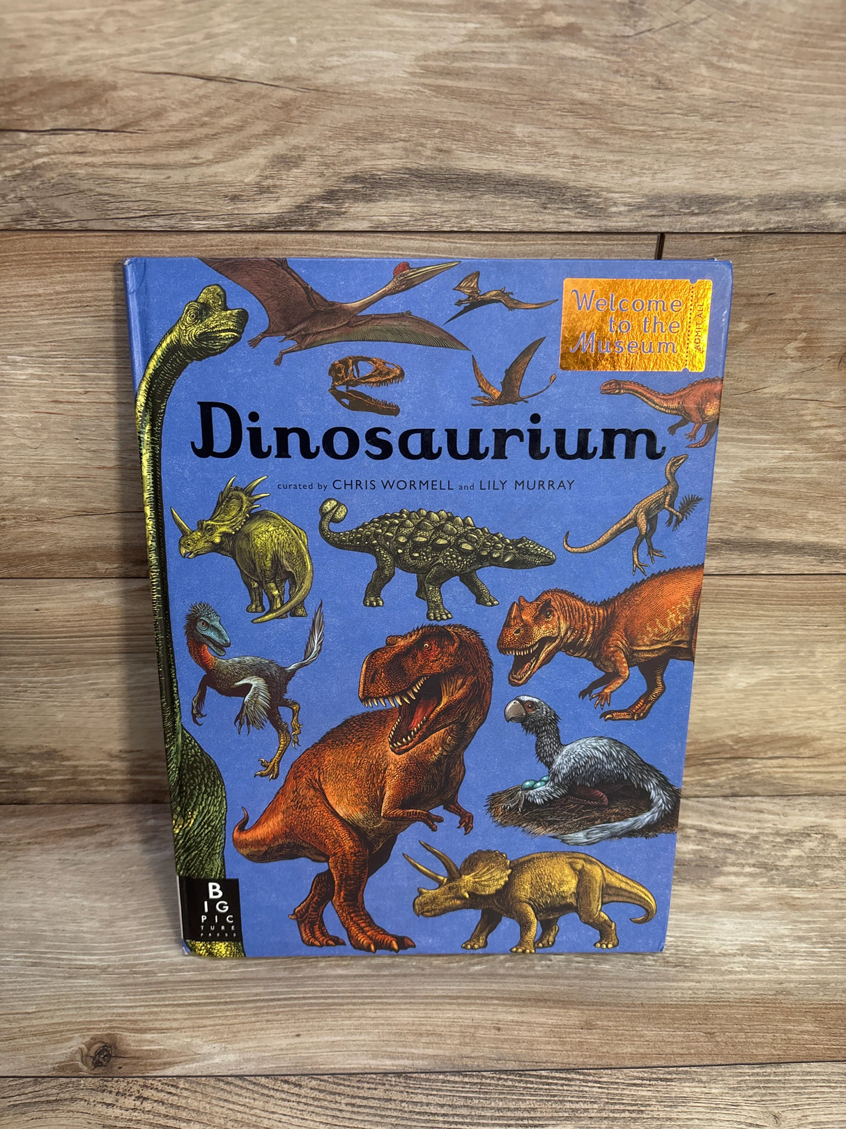 Dinosaurium book cover with illustrated dinosaurs on wood background, Welcome to the Museum series