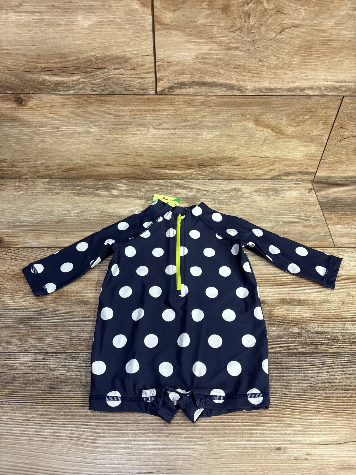 Front view of Primary rash guard romper showcasing navy and white polka dots, yellow half-zip, long sleeves, and snaps