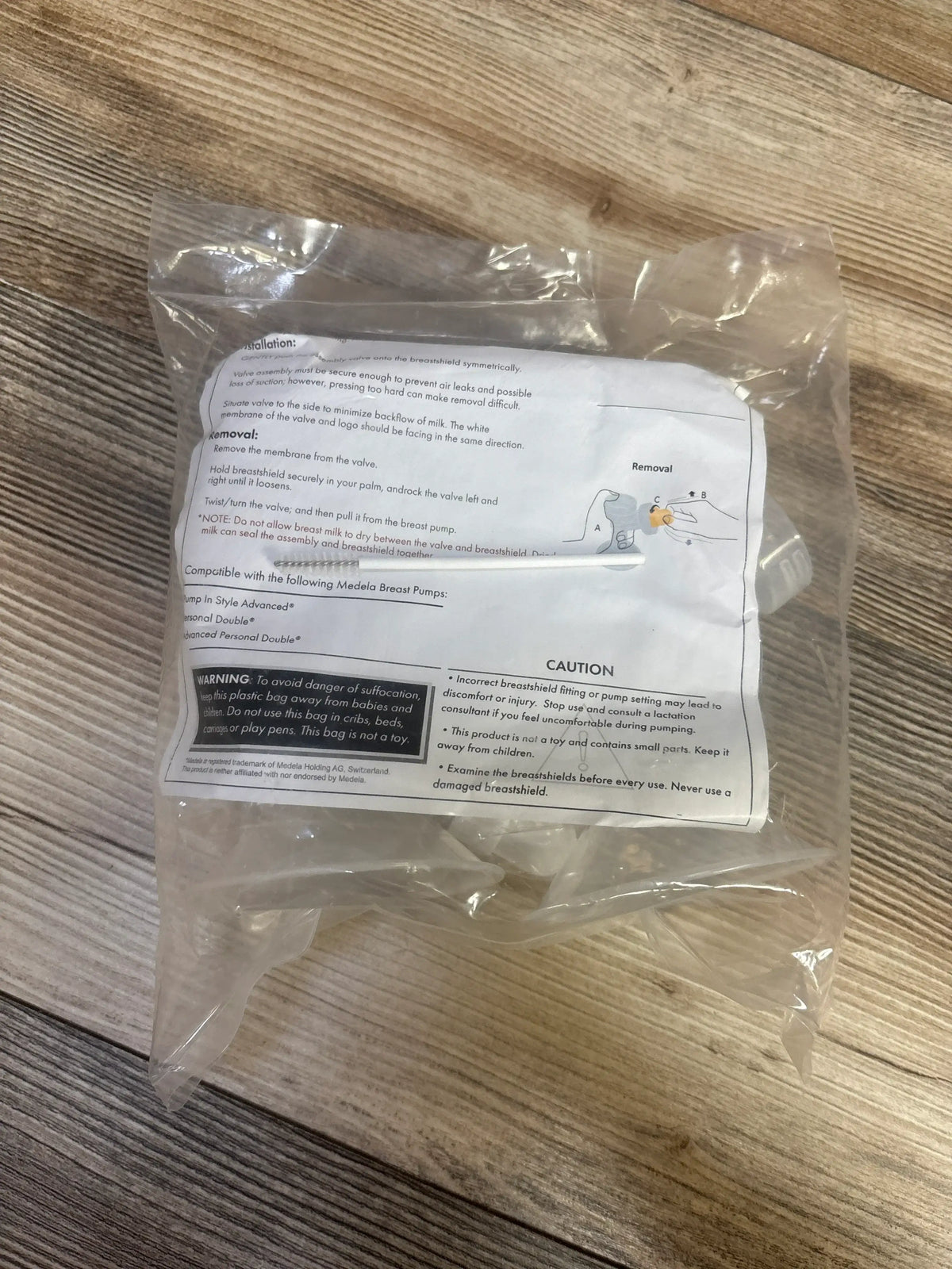 Angled view of Medela double pumping kit in sealed clear bag with instruction sheet and warning label on wood floor