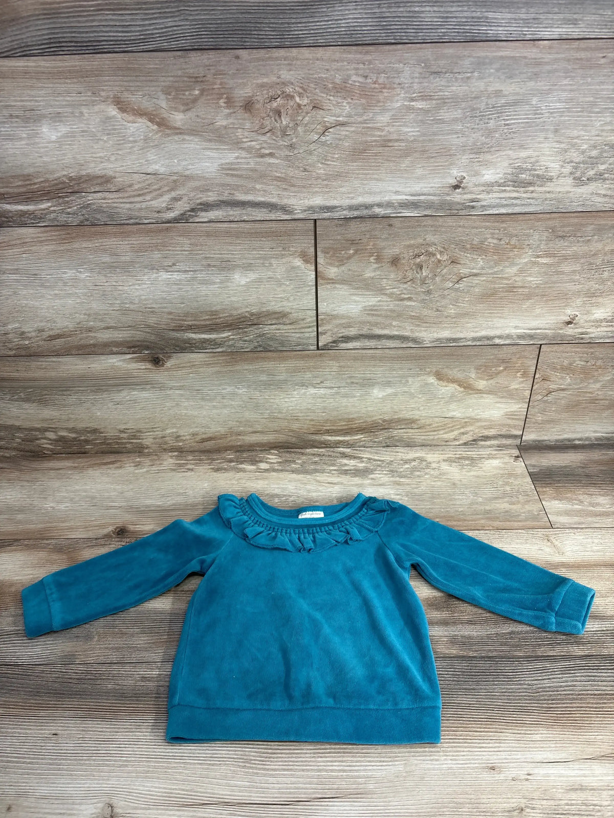 Blue long sleeve toddler shirt with ruffled neckline on wooden background