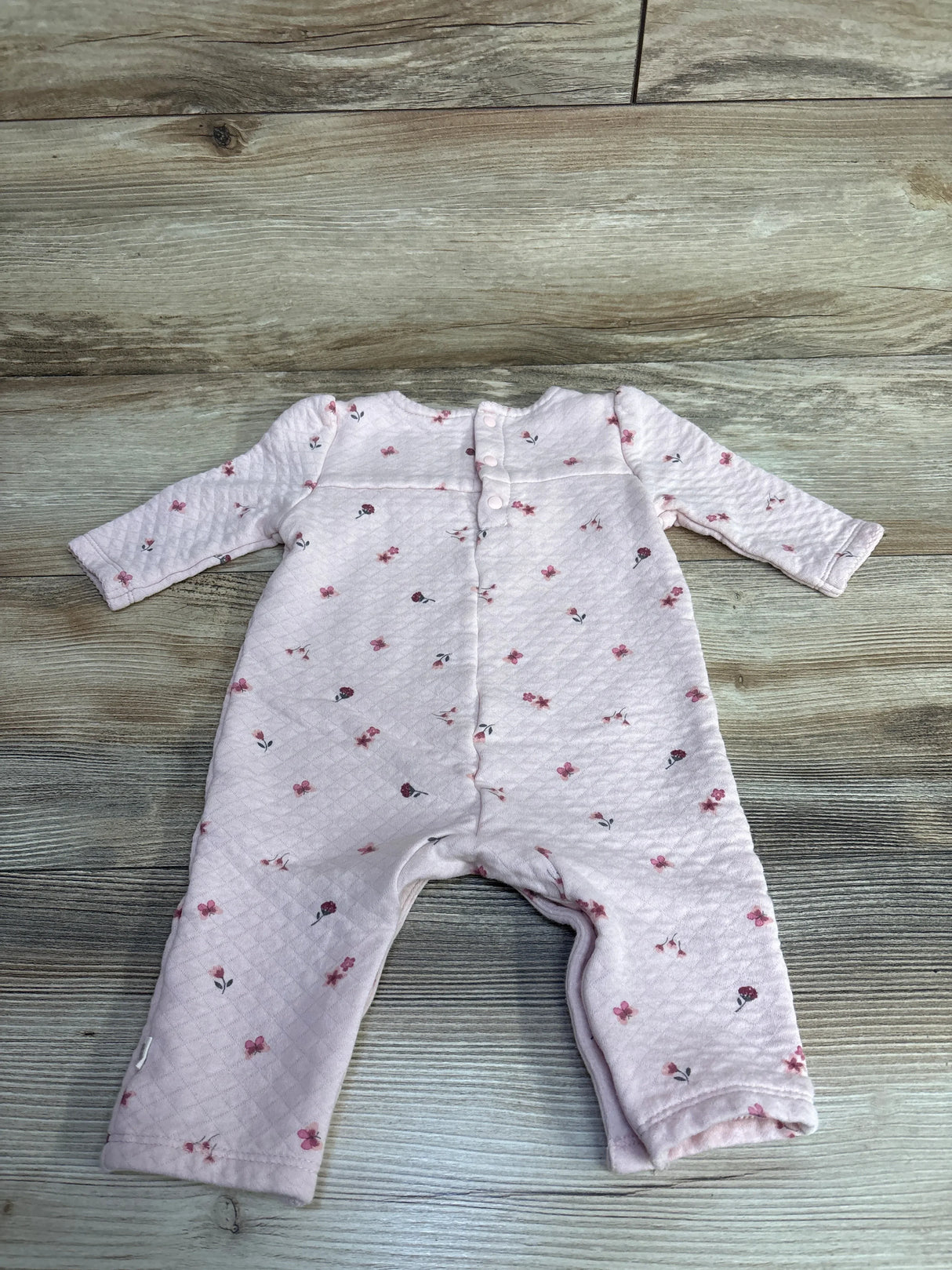Flat lay of Huggies Textured Floral Butterfly Coverall Pink sz 6m showcasing pink quilted long sleeve coverall with floral print on wood plank floor
